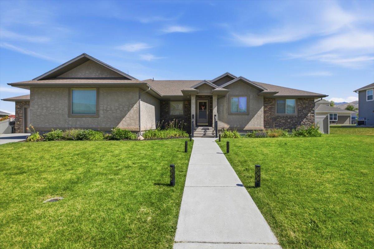 Contemporary ranch-style residence featuring a stucco and stone facade, a concrete walkway with integrated path lighting, an attached garage, a covered entry, and established landscaping