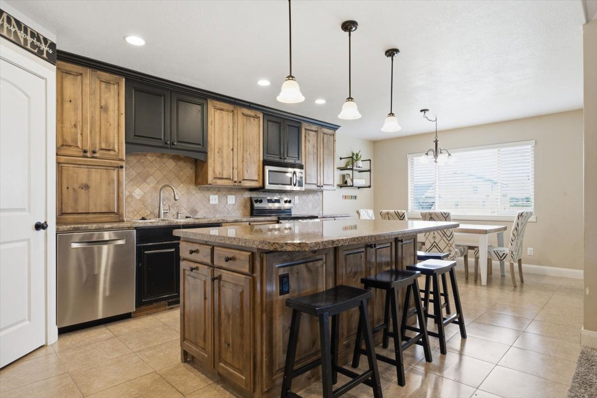 Kitchen featuring an oversized island with a stone countertop, a tile backsplash, stainless steel appliances, and two-tone cabinetry