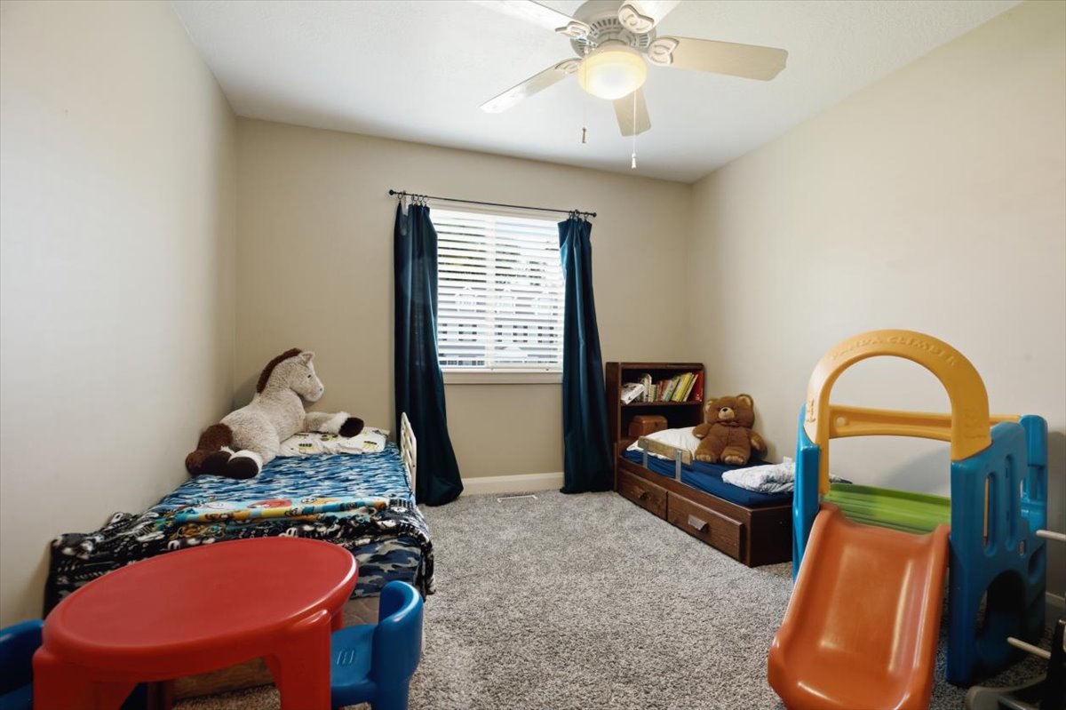 Bedroom featuring light neutral wall tones, grey textured carpeting, and a ceiling fan with integrated lighting