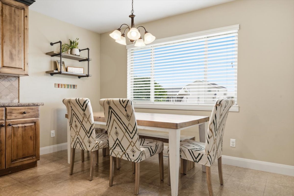 Dining area featuring a single-pane window with horizontal blinds, a traditional multi-bulb chandelier, and tiled flooring