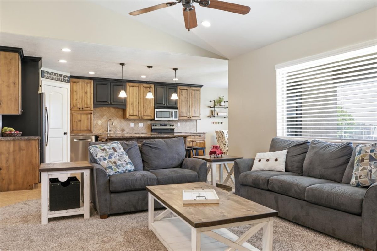 Open-concept living space featuring vaulted ceilings with a ceiling fan, recessed lighting, and a large window with blinds