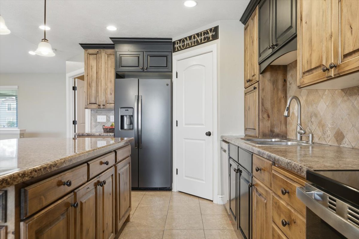 Kitchen featuring a large island with stone-finish countertop, dual-tone cabinetry with black and natural wood finishes, and a stainless steel refrigerator