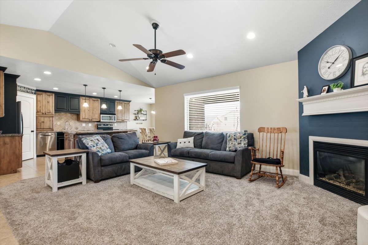 Open-concept living space featuring vaulted ceilings, a ceiling fan, and a fireplace with a white mantel