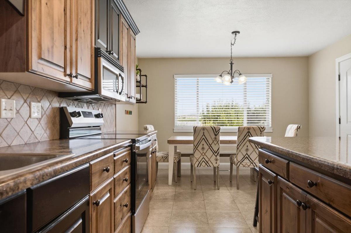 Kitchen featuring wood cabinetry, stainless steel appliances, tiled backsplash, and a dining area with a chandelier