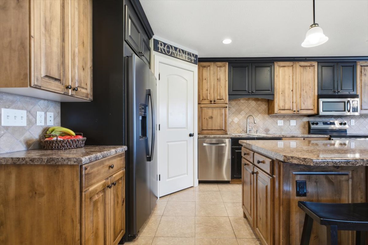 Kitchen featuring two-tone cabinetry with natural wood and dark finishes, granite-look countertops, and stainless steel appliances including a refrigerator, dishwasher, and microwave