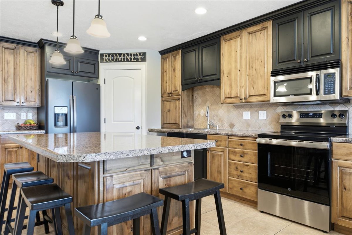 Kitchen featuring a breakfast bar with stone countertops, a full suite of stainless steel appliances, two-tone cabinetry, and a tile backsplash