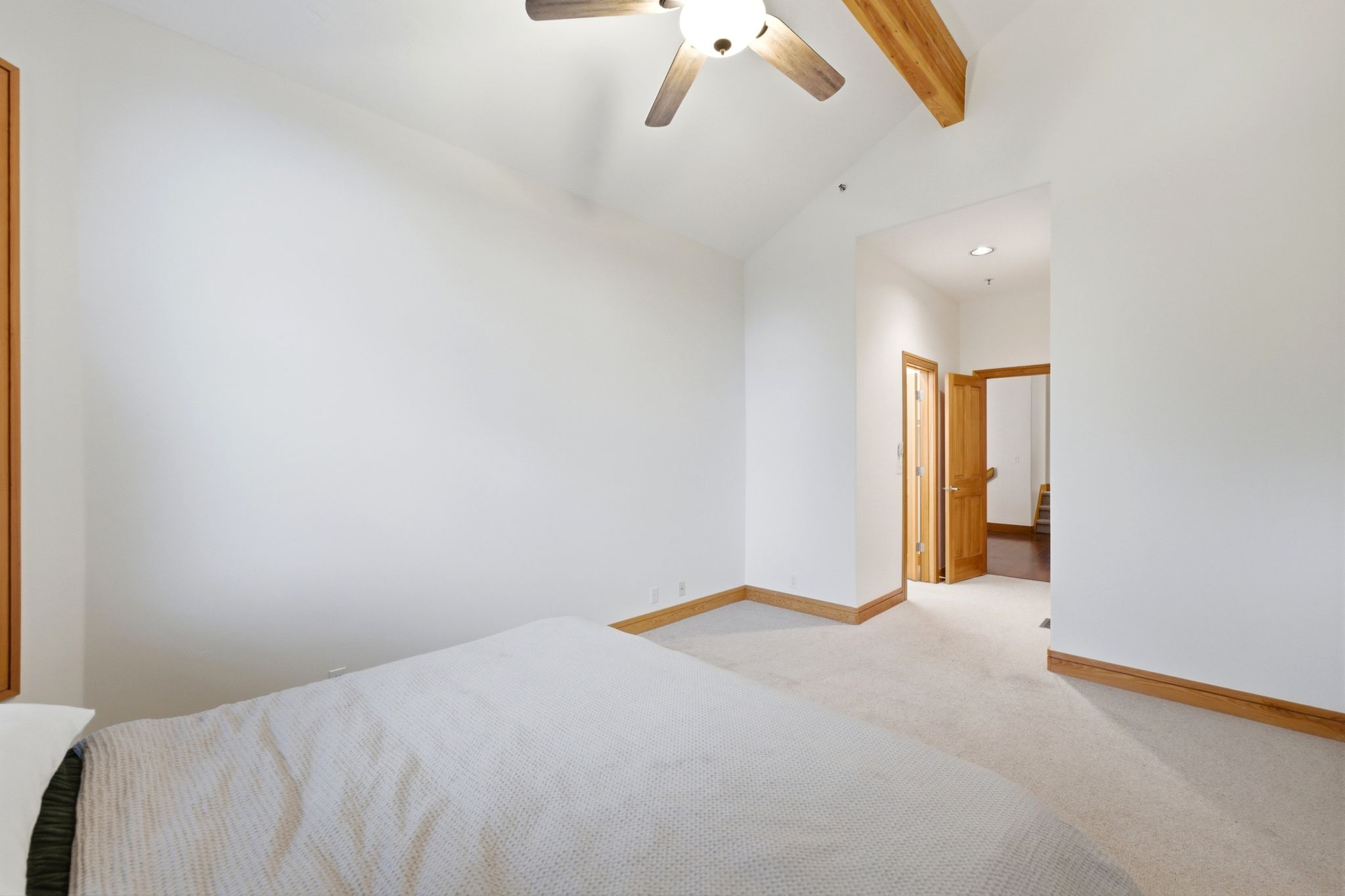 Spacious room featuring vaulted ceilings with exposed wood beams, a ceiling fan with integrated lighting, and light-toned carpet flooring