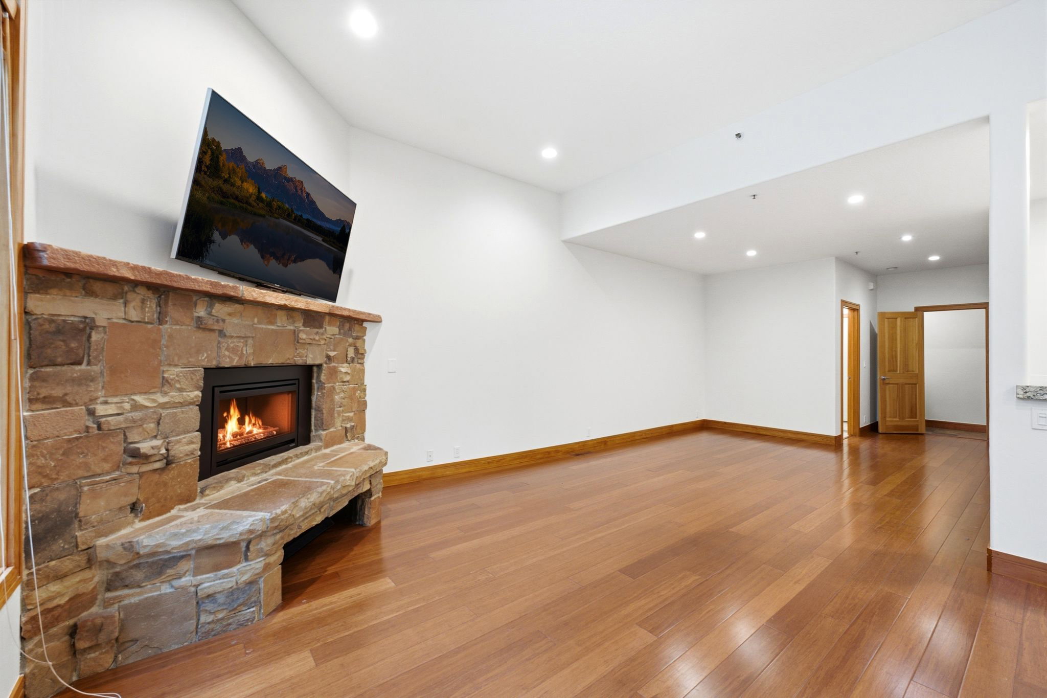 Living area featuring a natural stone fireplace with an integrated stone bench, hardwood flooring, recessed lighting, and white walls