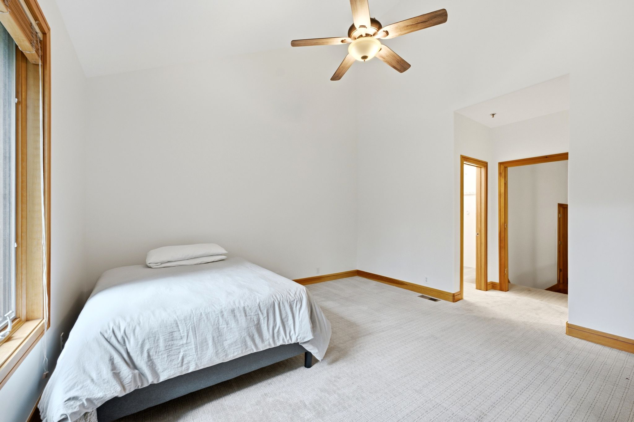 Carpeted room featuring a ceiling fan with light fixture, natural wood trim, and a window with wood-finish casing