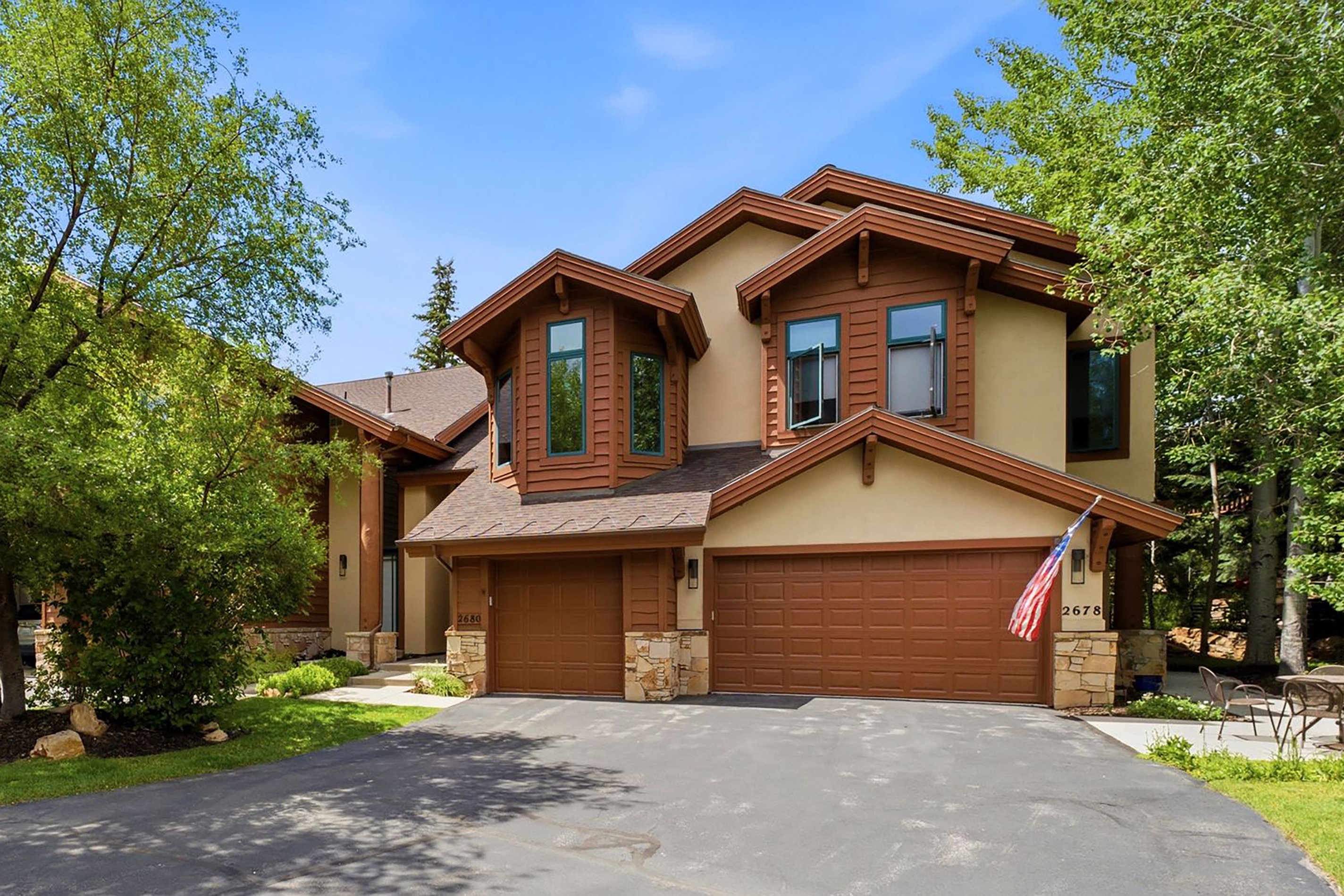 Multi-level stucco exterior featuring brown trim accents, a dual garage, stone pillars, and a paved driveway