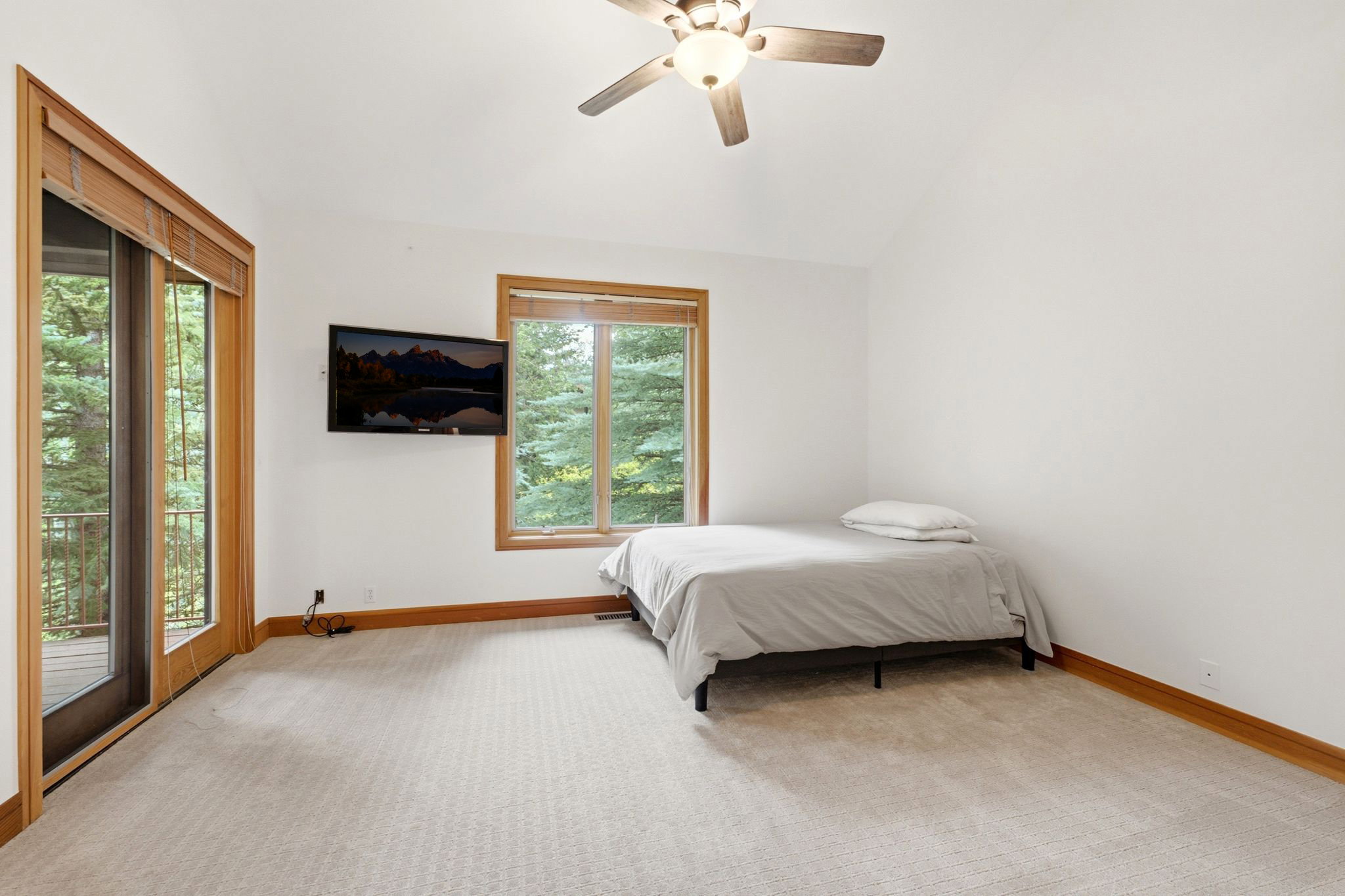 Vaulted ceiling room featuring light-toned carpet flooring, a ceiling fan with integrated lighting, and wood-framed windows