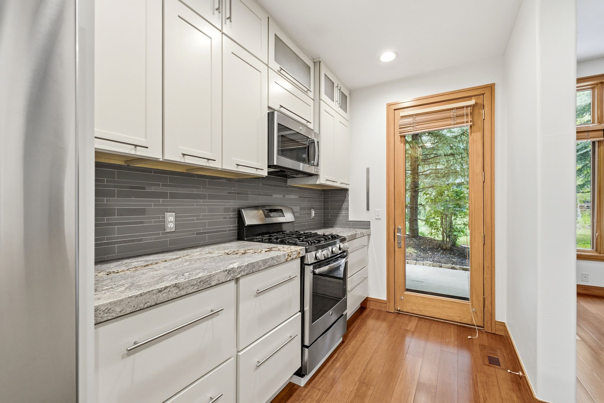 Kitchen featuring light-finish cabinetry, stainless steel appliances, a horizontal tile backsplash, and stone countertops