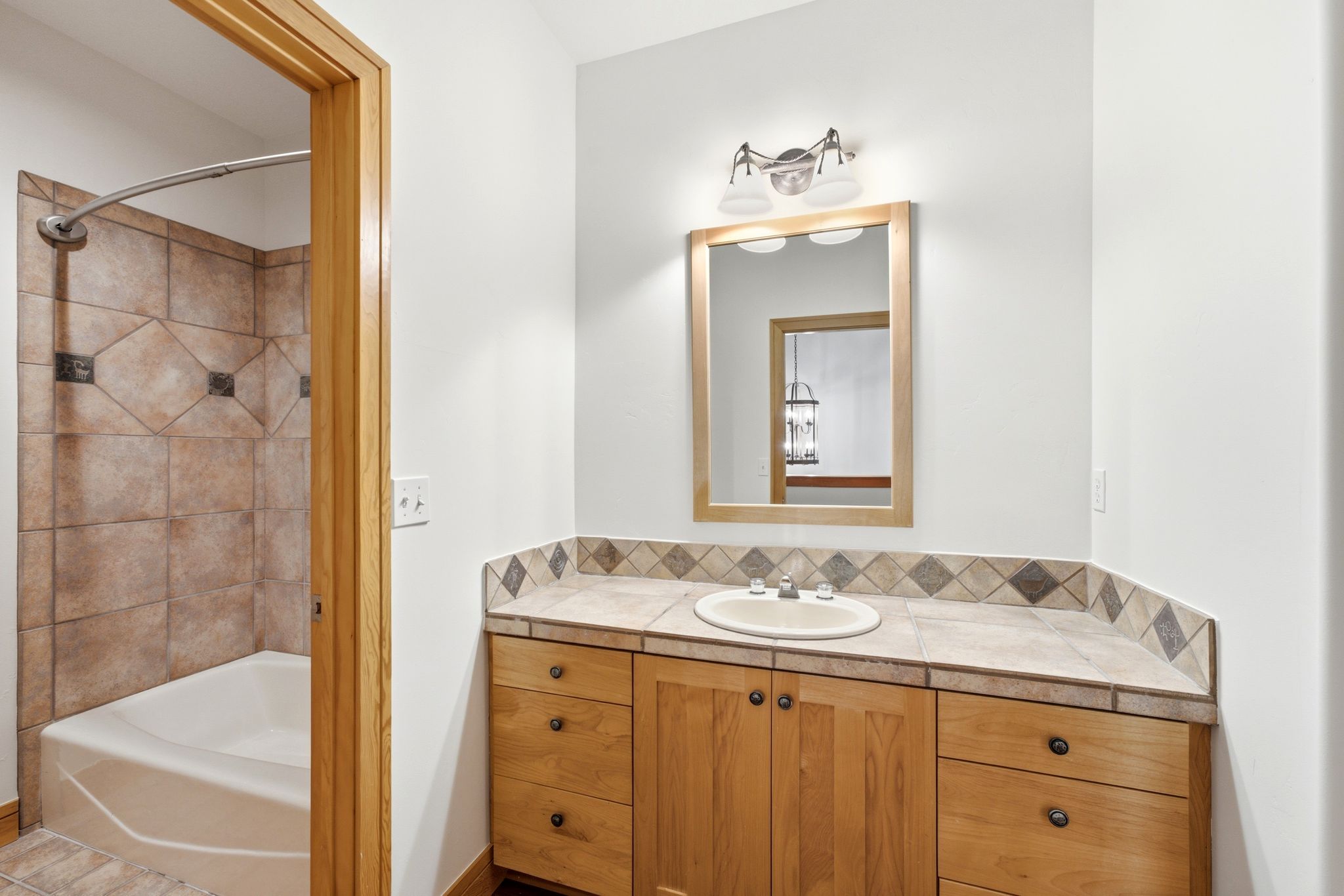 Bathroom vanity featuring wood cabinetry, tile countertop, and a framed mirror with overhead lighting