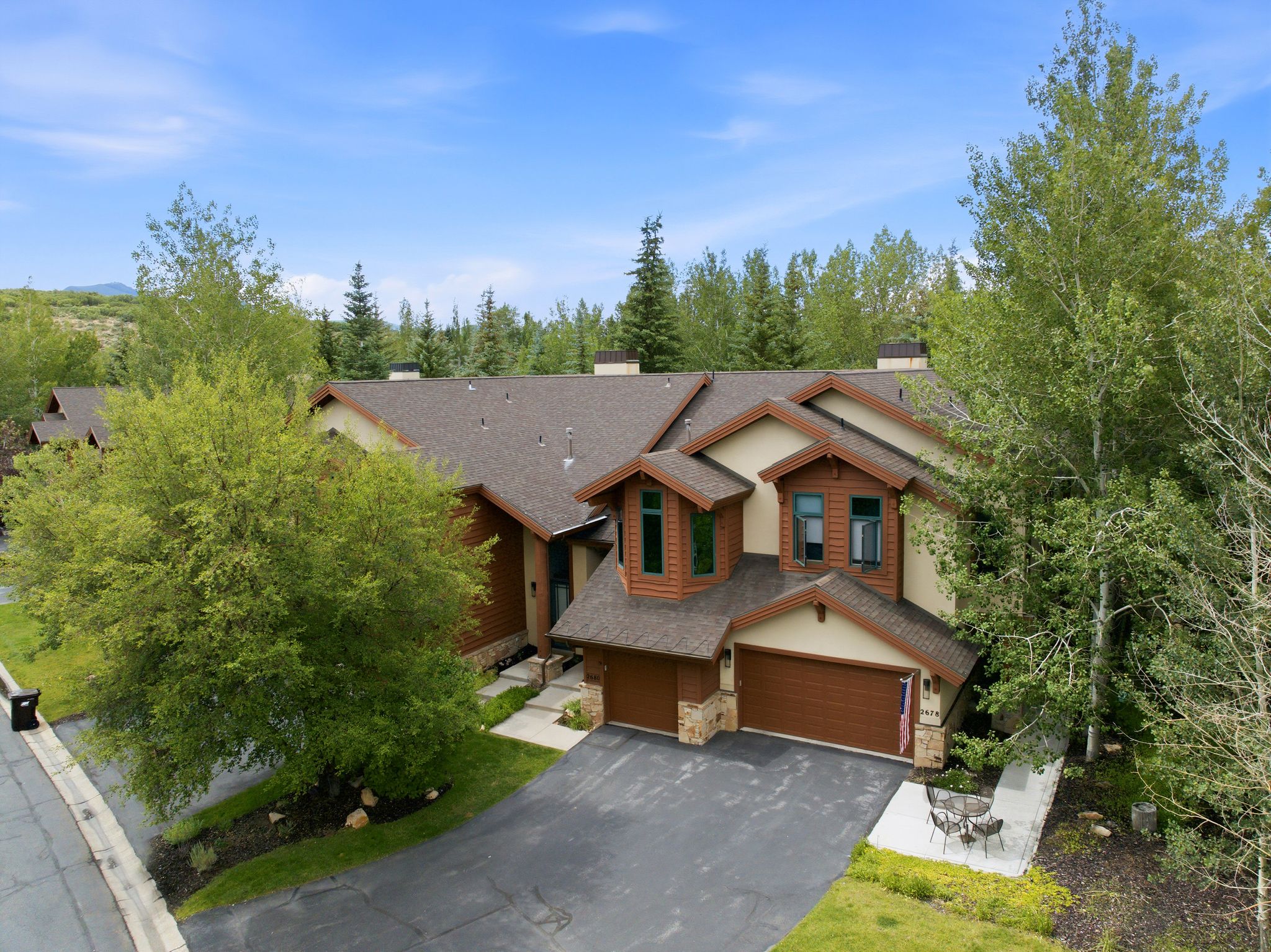 Multi-level property featuring a brown shingle roof and light-colored stucco siding with wood accents
