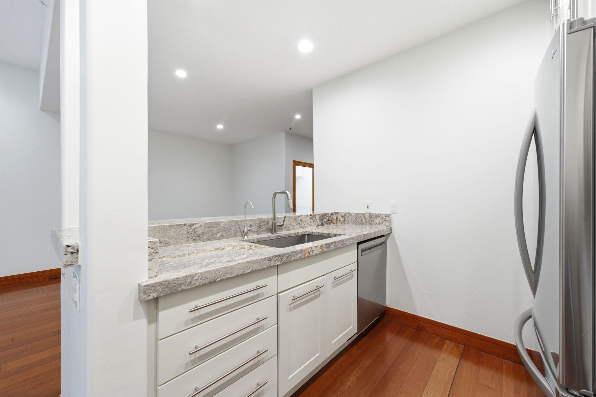 Kitchenette featuring light-colored cabinetry, stainless steel sink with gooseneck faucet, light granite countertops, and wood-finish flooring