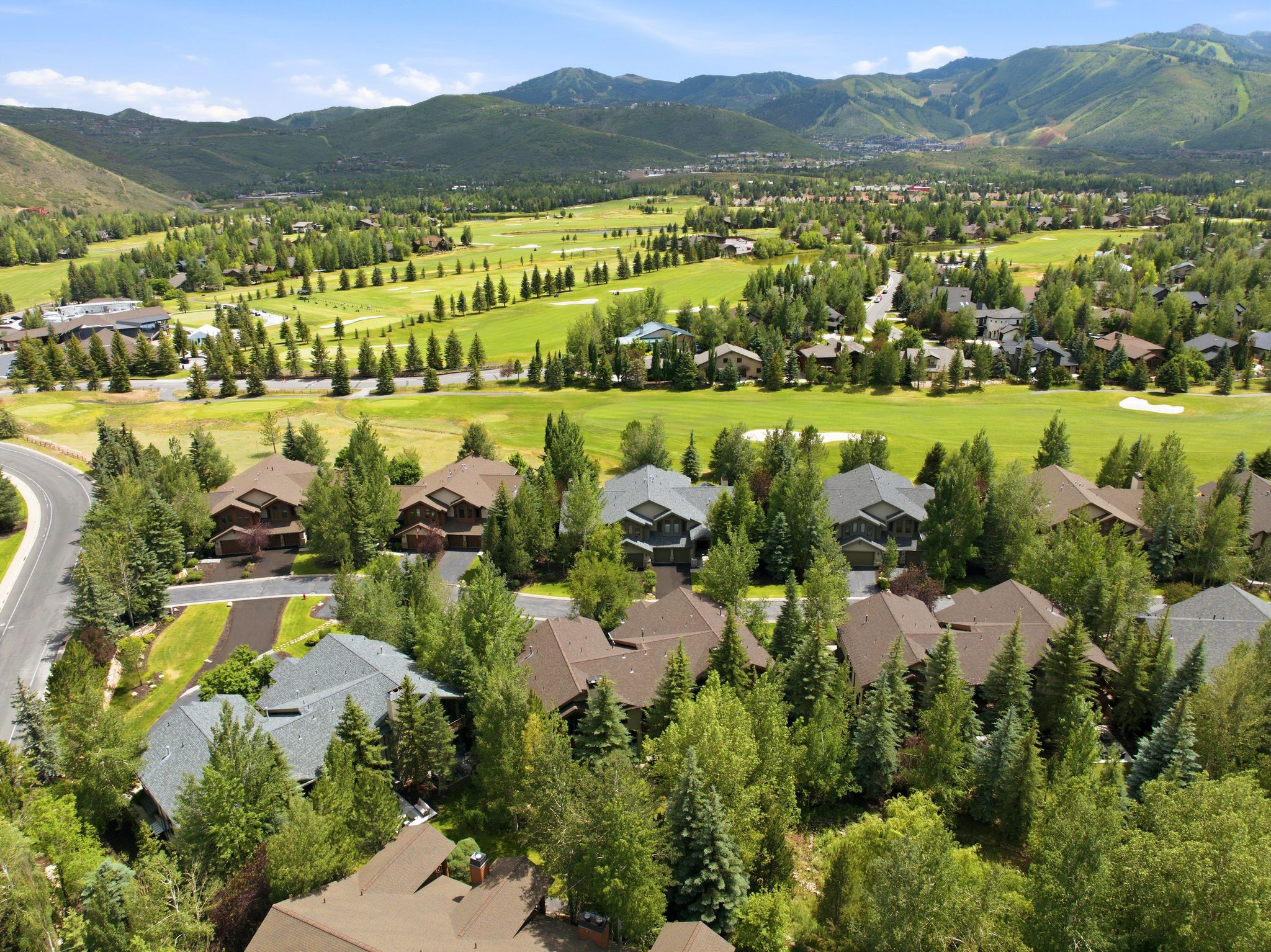 Expansive residential community featuring a golf course, abundant mature trees, paved roads, varied architectural styles, and distant mountains