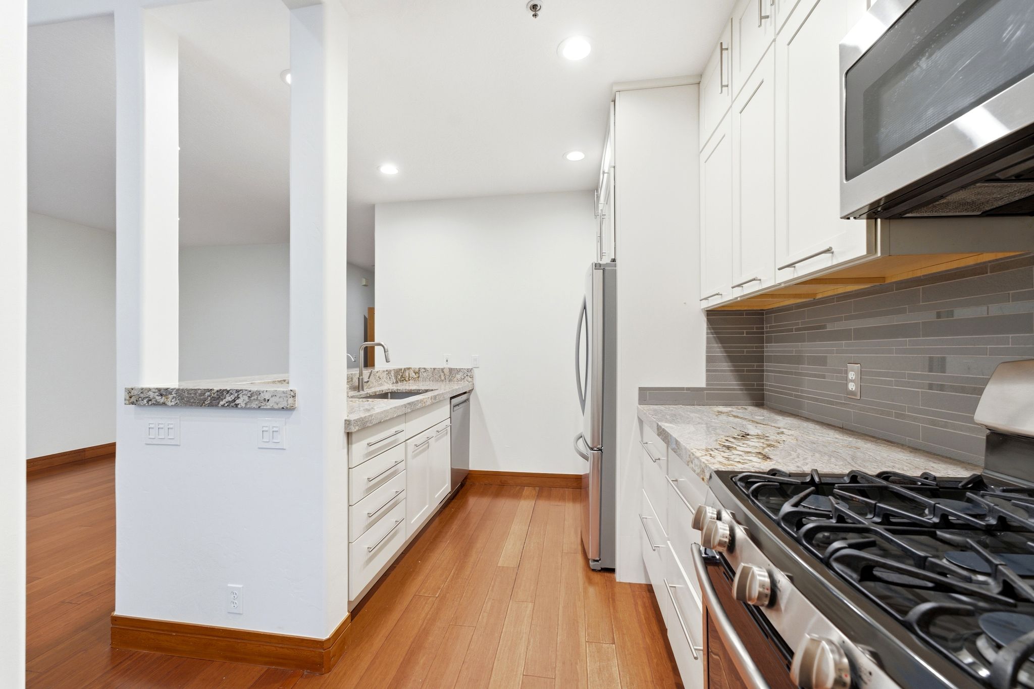 Modern kitchen featuring white cabinetry, stainless steel appliances, and wood-finish flooring