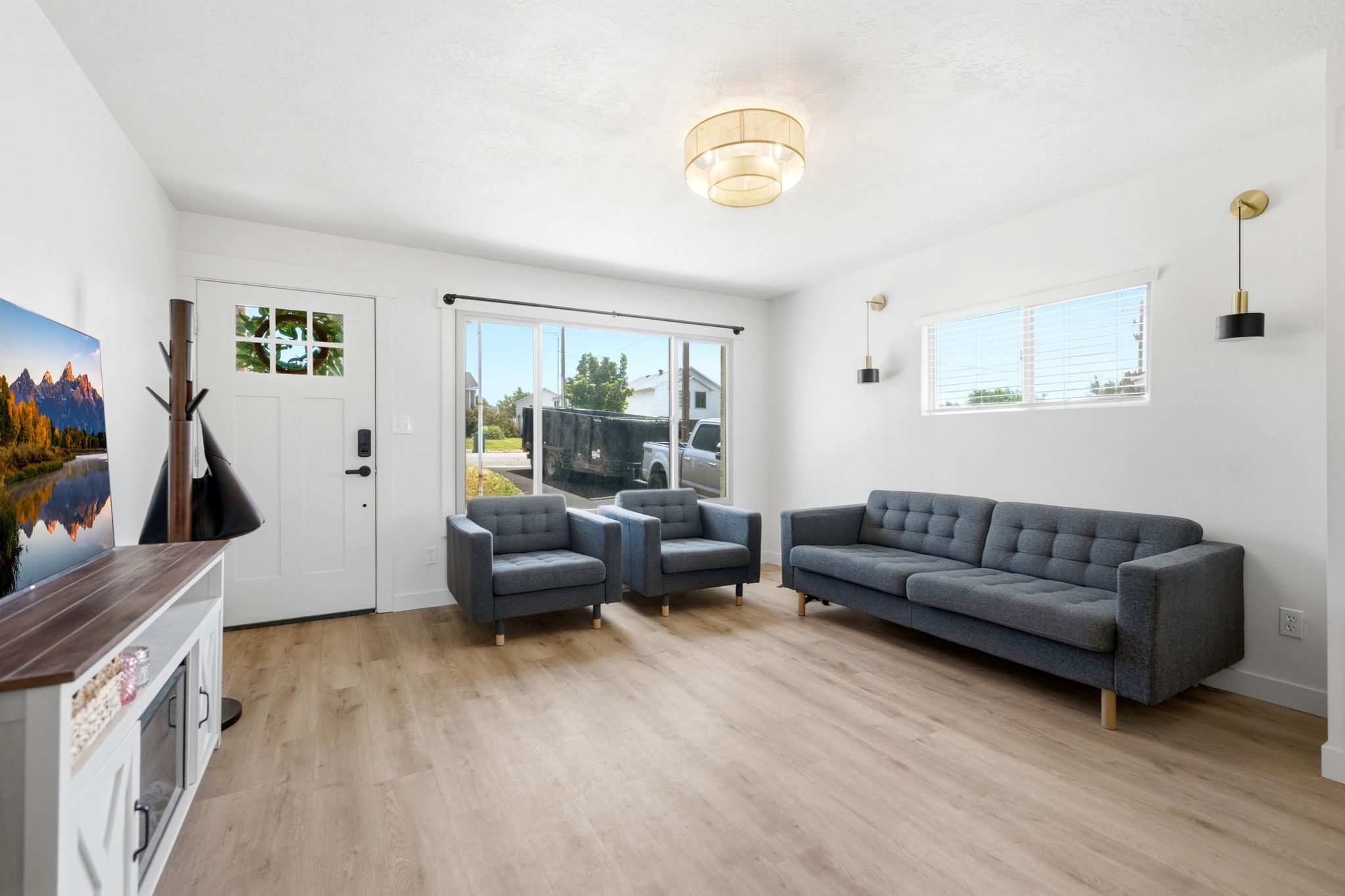 Spacious living area featuring light wood-finish flooring, a white paneled entry door with decorative glass inserts, and a sliding glass door