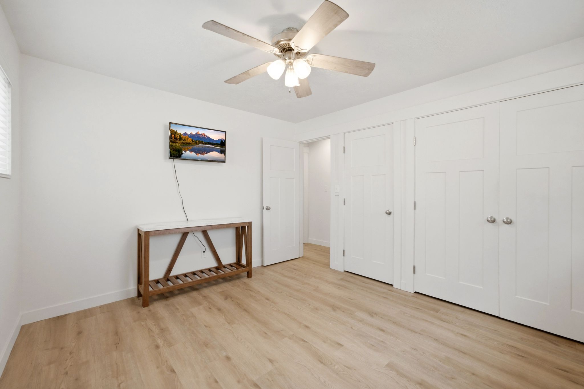 Light wood-finish flooring complemented by white walls, a ceiling fan, and multiple white paneled doors
