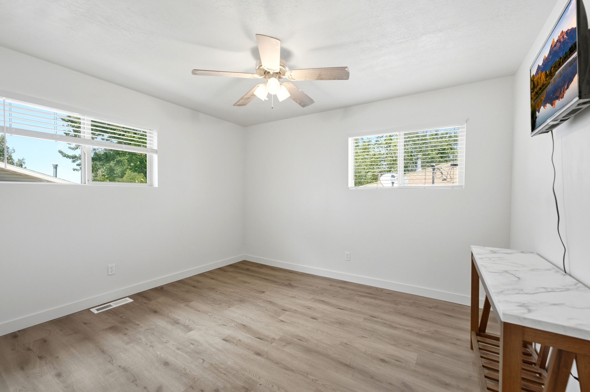 Bright room featuring wood-finish flooring, white walls, and a ceiling fan