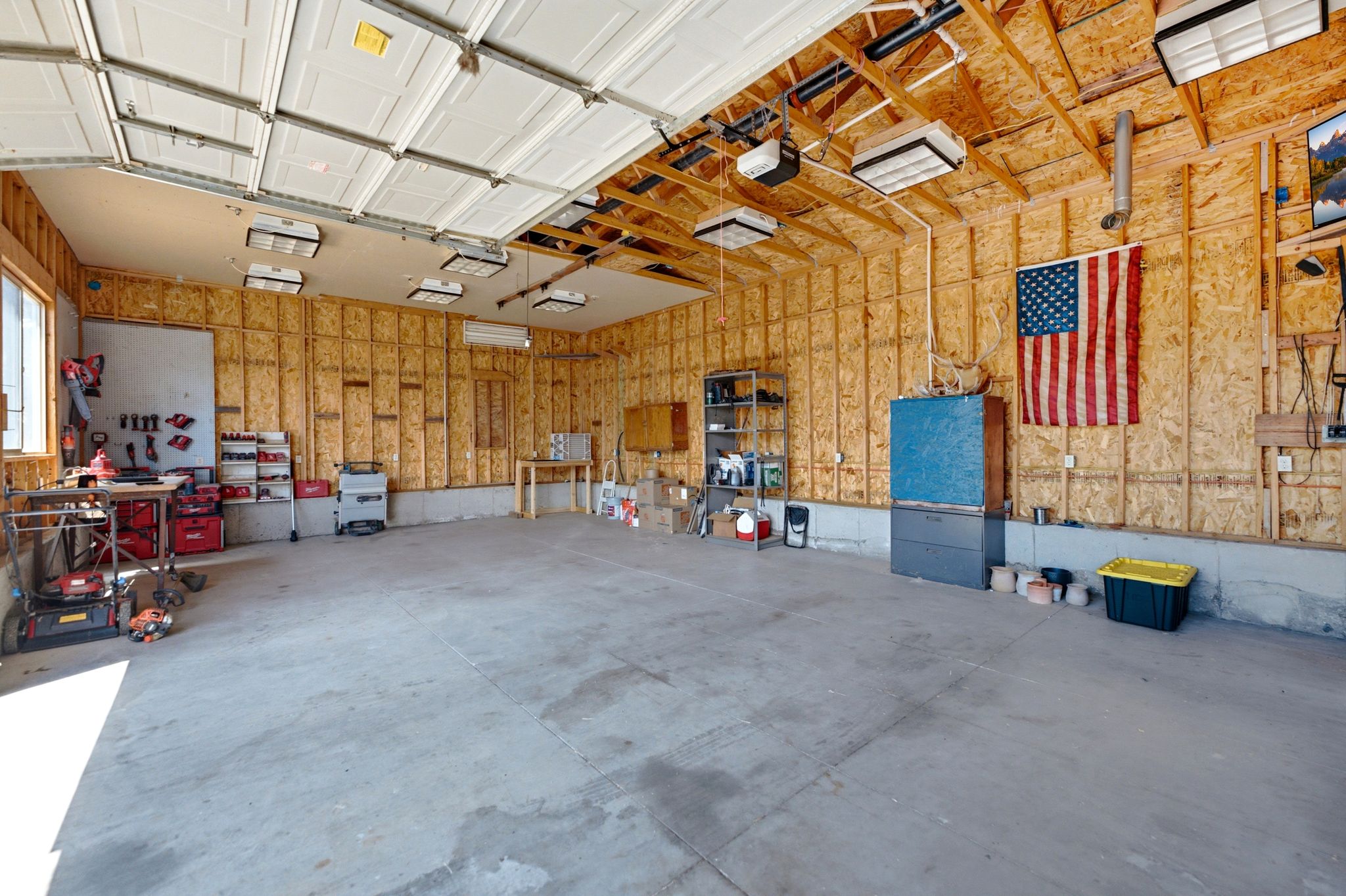 Spacious garage featuring a concrete floor, exposed wood framing, multiple overhead lighting fixtures, and a large garage door