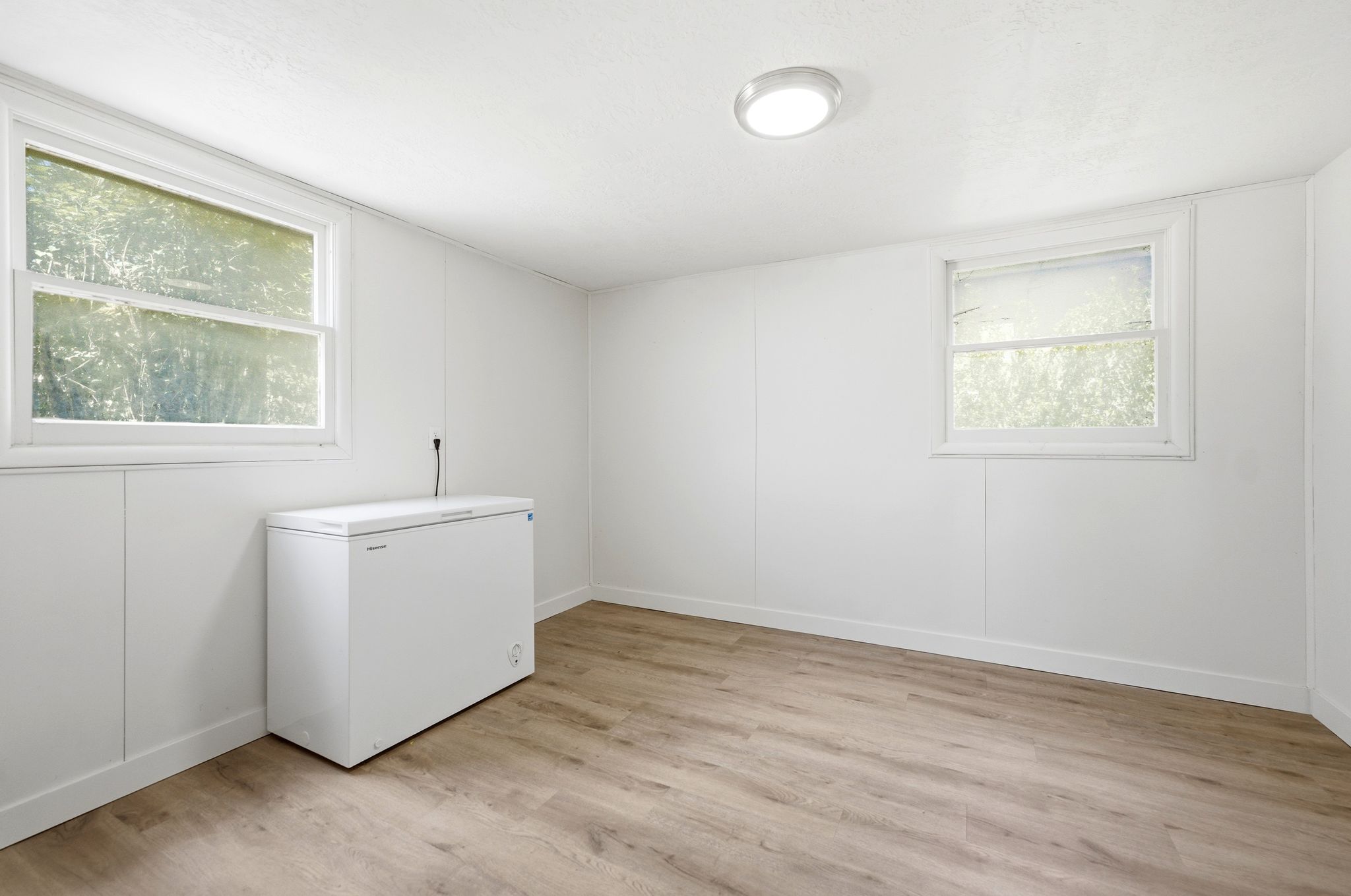 Room featuring wood-finish flooring, white paneled walls, and two windows