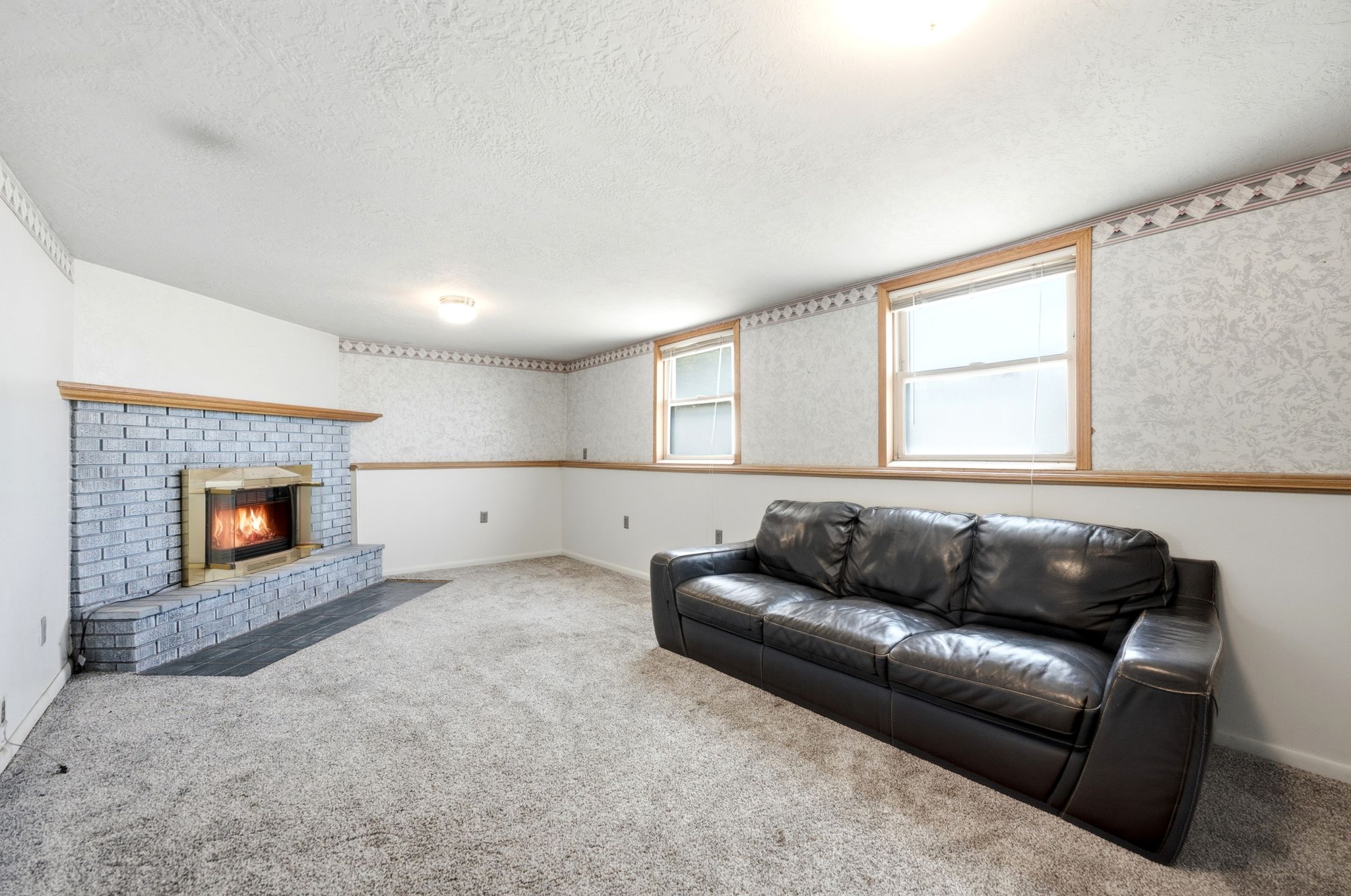 Spacious room featuring a brick-surround fireplace with a wood mantle, soft carpet flooring, and two windows with wood trim