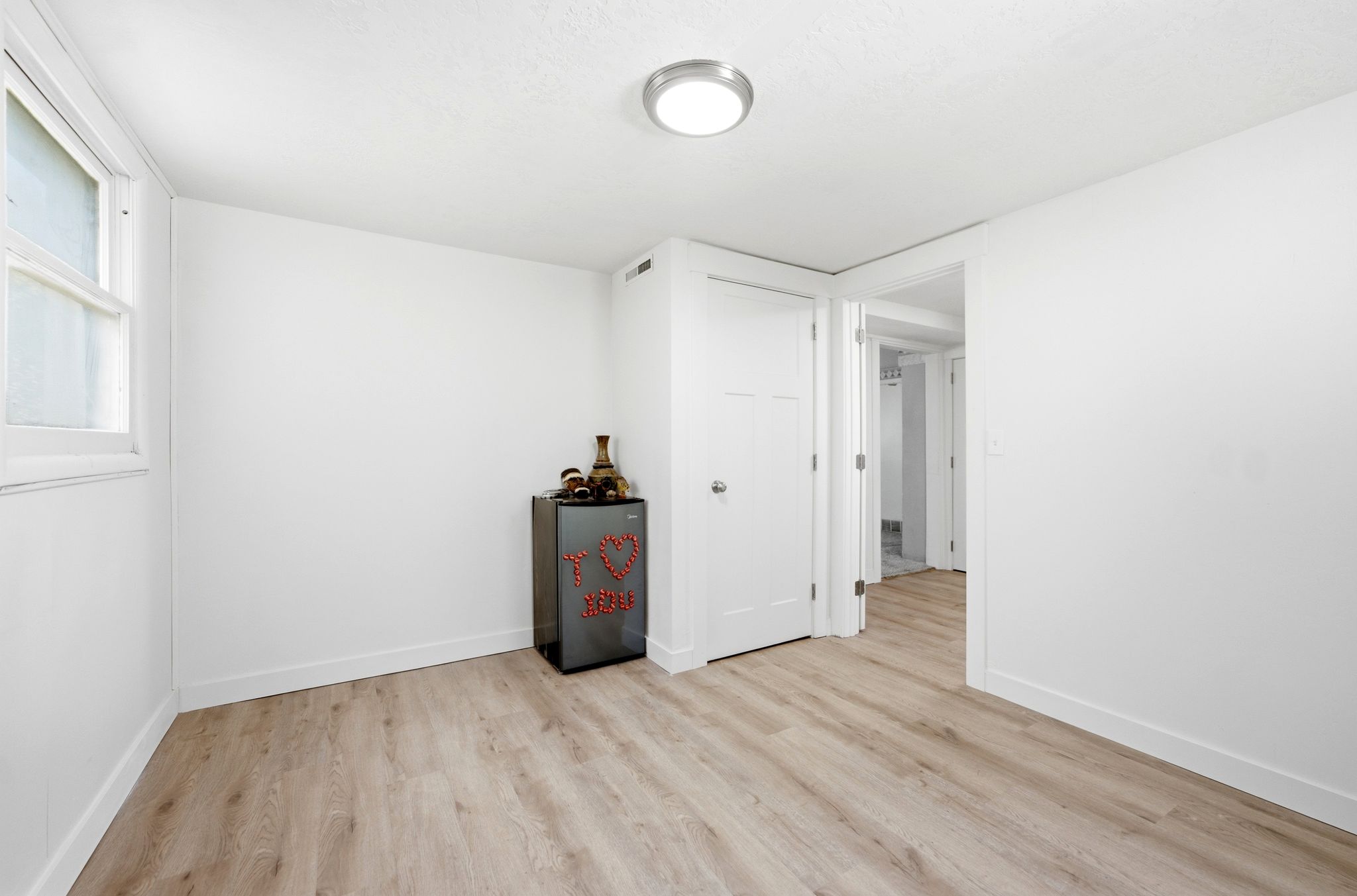 Room featuring wood-finish flooring, white walls, and a window with white trim