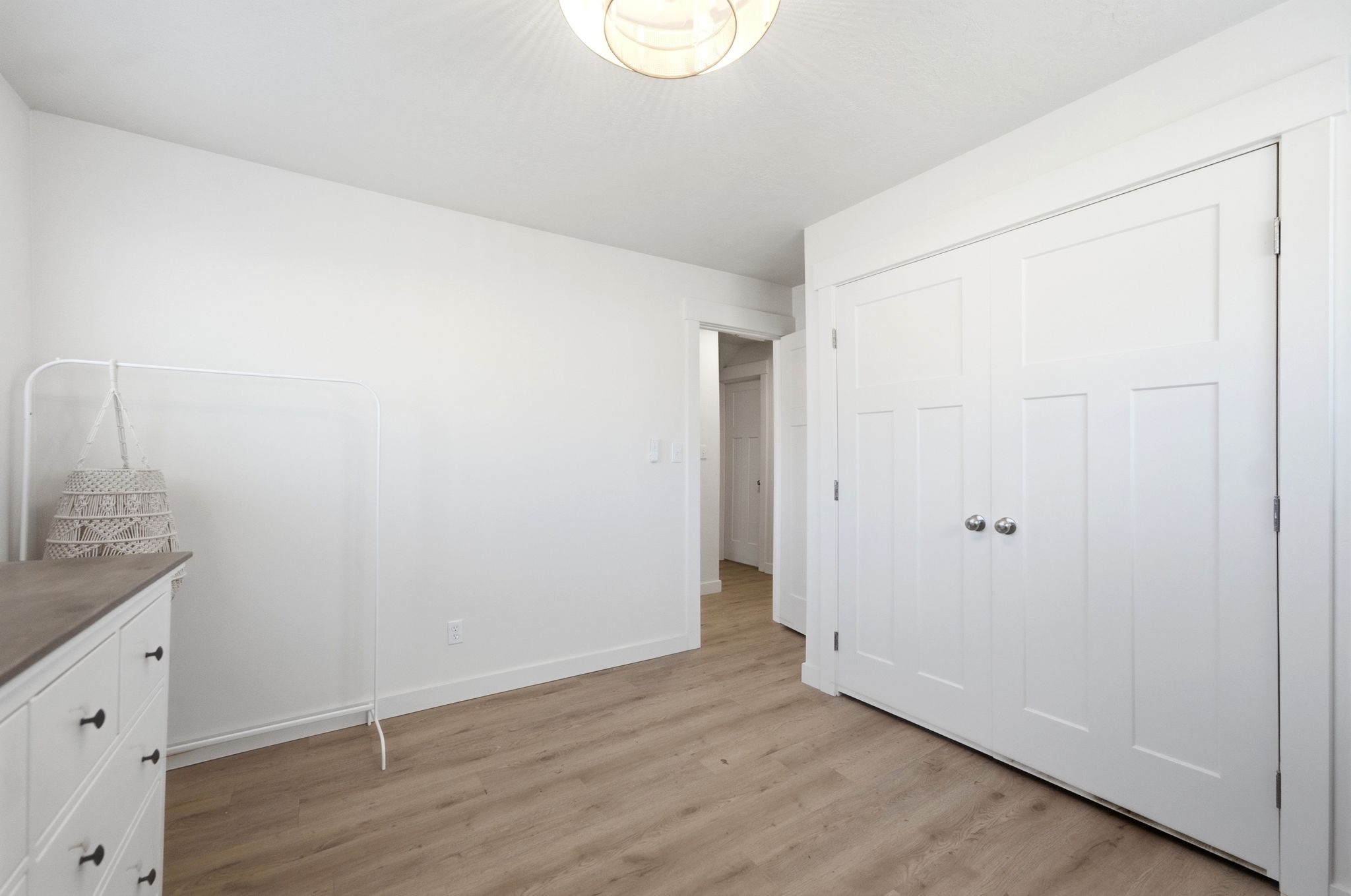Room with light wood-finish flooring, white walls, and a contemporary ceiling light fixture