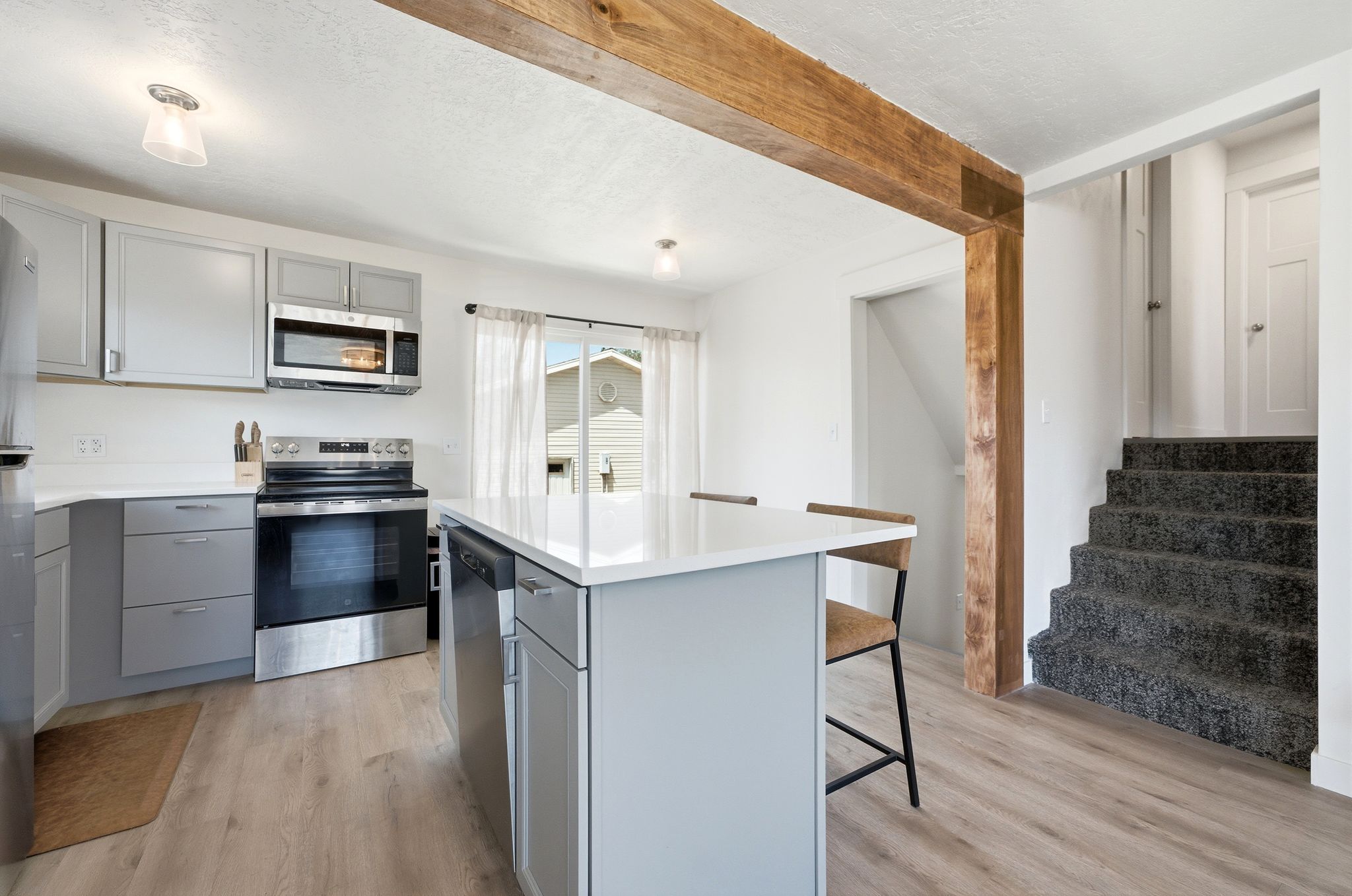 Contemporary kitchen featuring light gray cabinetry, stainless steel appliances, and a central island with a white countertop