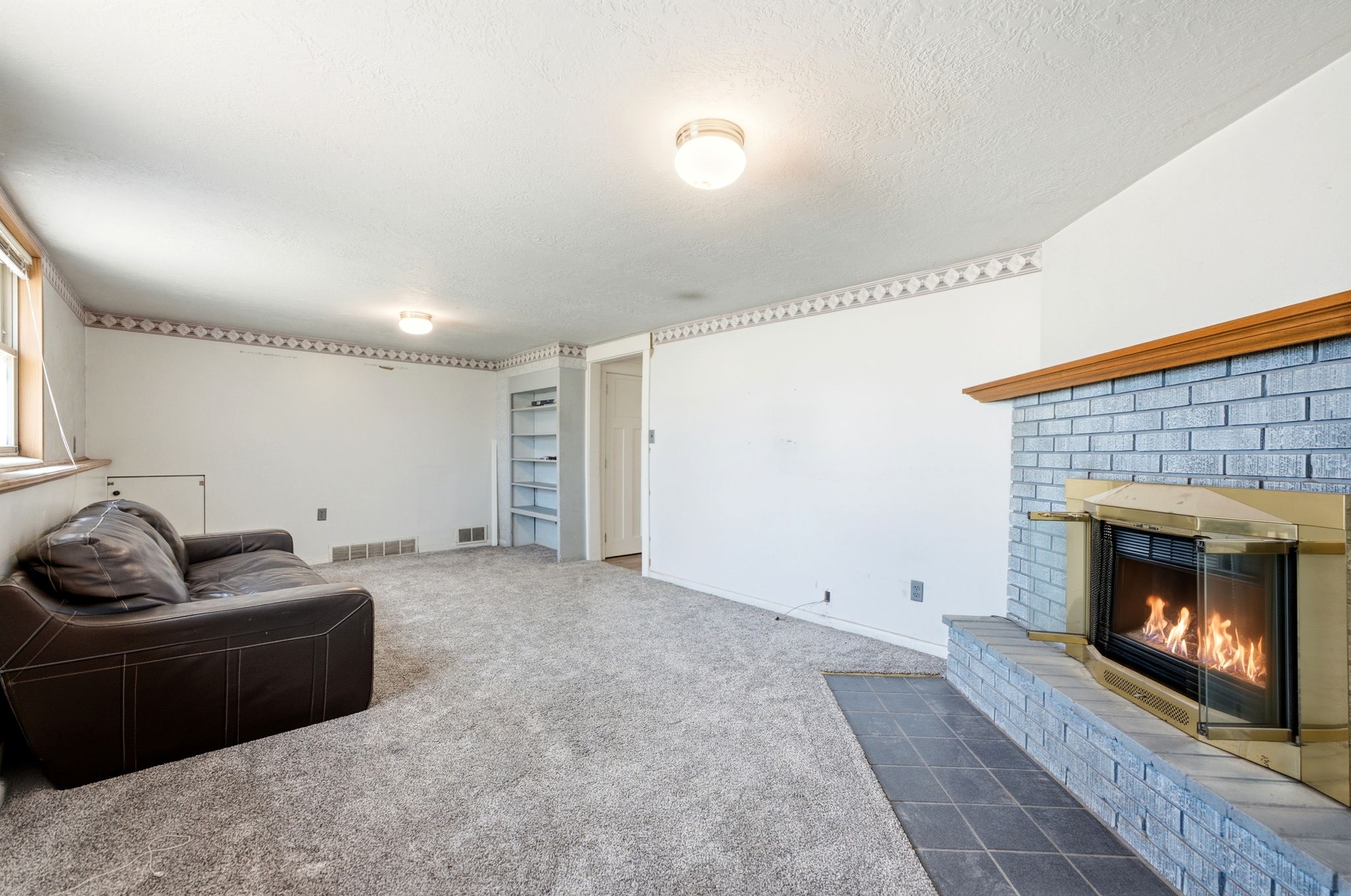 Living area featuring a brick fireplace with a wood mantle, an integrated built-in shelving unit, and wall-to-wall carpeting