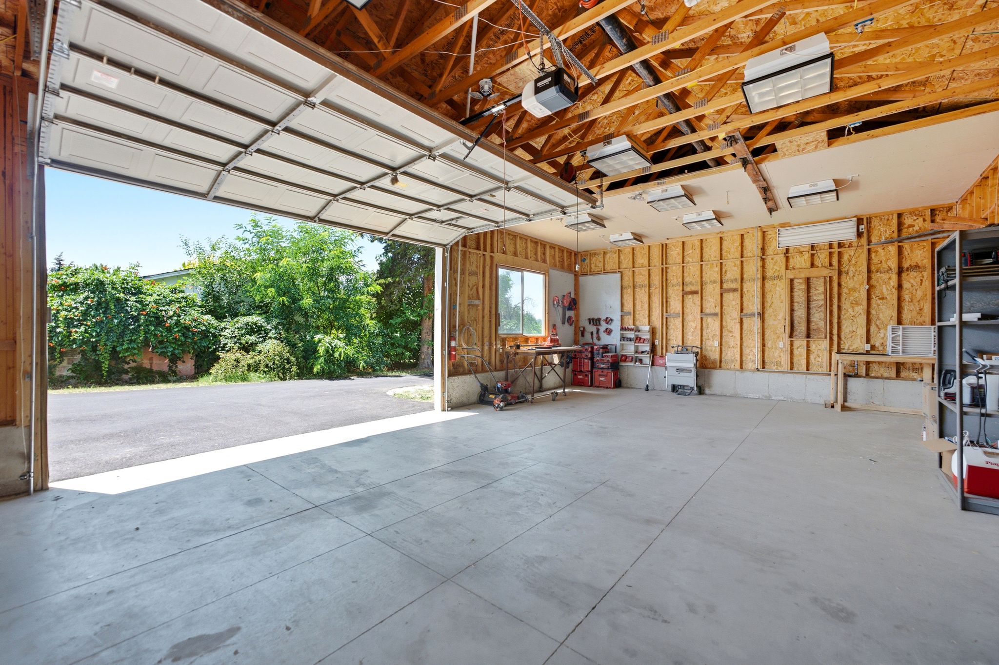 Spacious garage with concrete flooring, exposed wood framing, and multiple overhead light fixtures