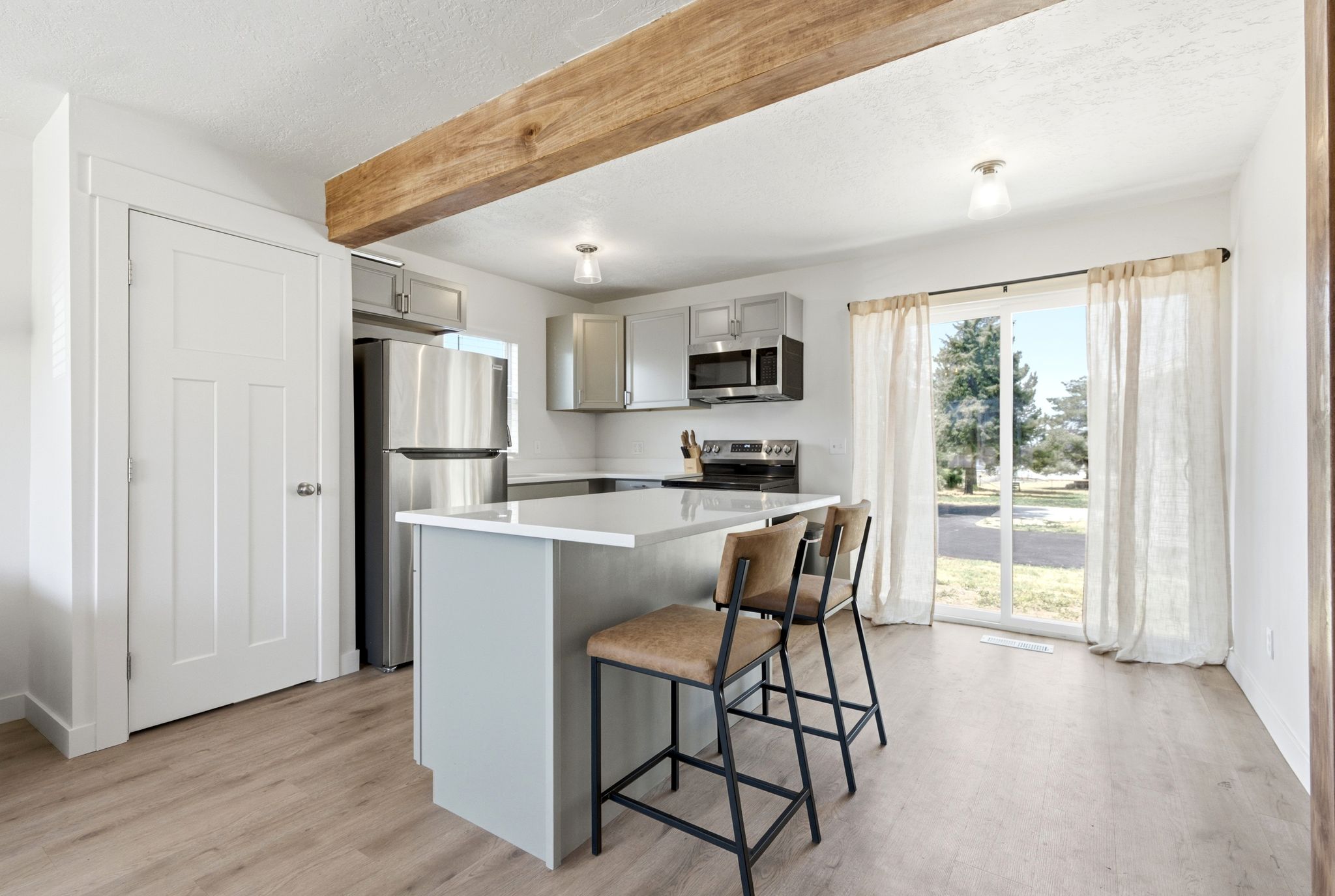 Kitchen featuring light wood-finish flooring, a wood beam ceiling accent, a center island with a white countertop, and stainless steel appliances