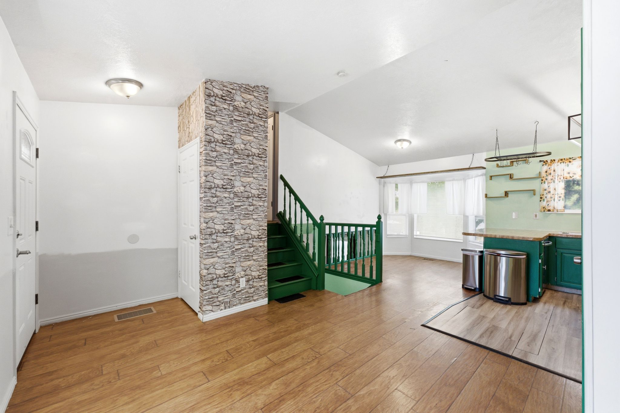 Open-concept living area featuring wood-finish flooring, a stone-accented wall, and a staircase with green railings