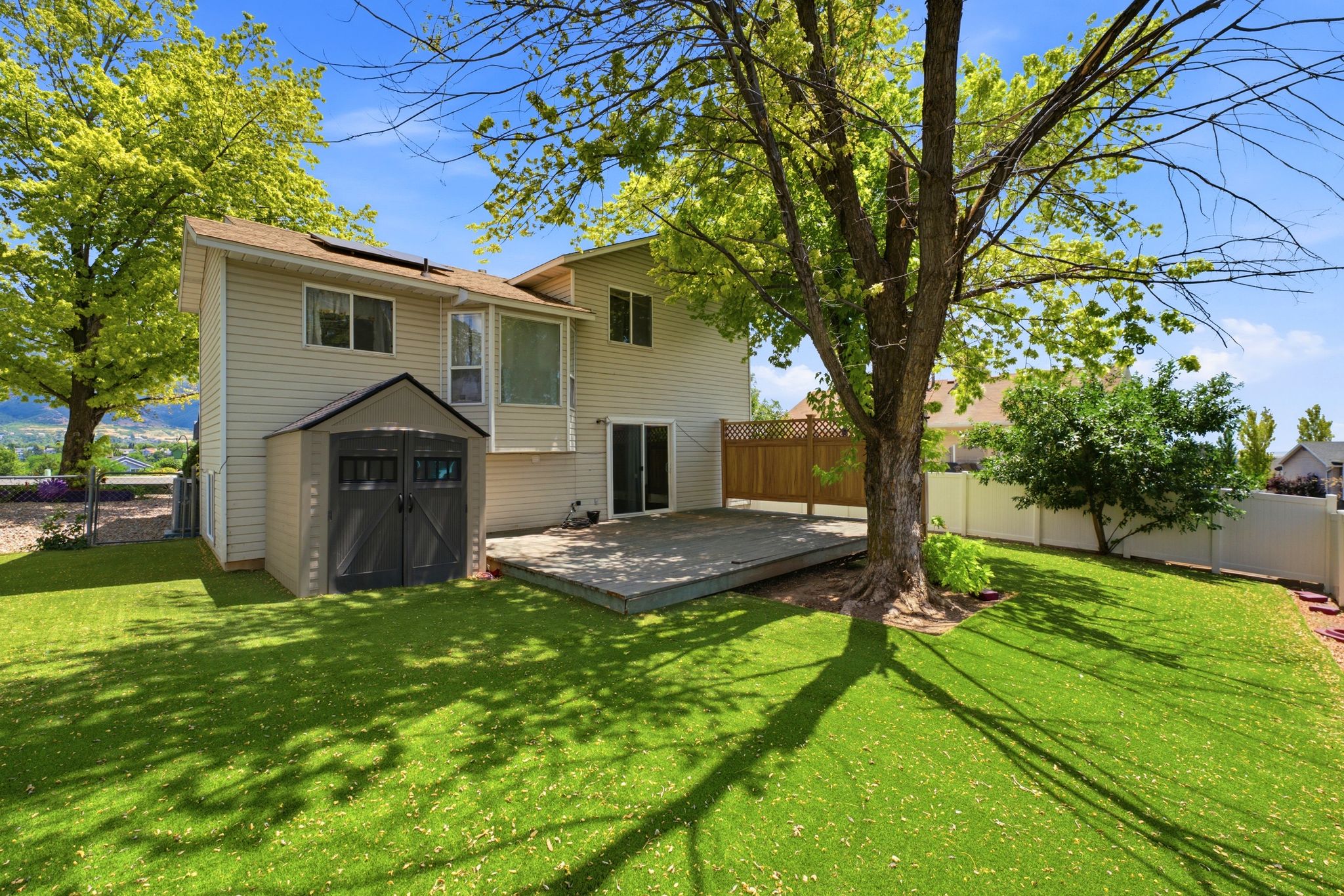 Expansive backyard featuring a large wooden deck, mature shade tree, manicured lawn, and a storage shed