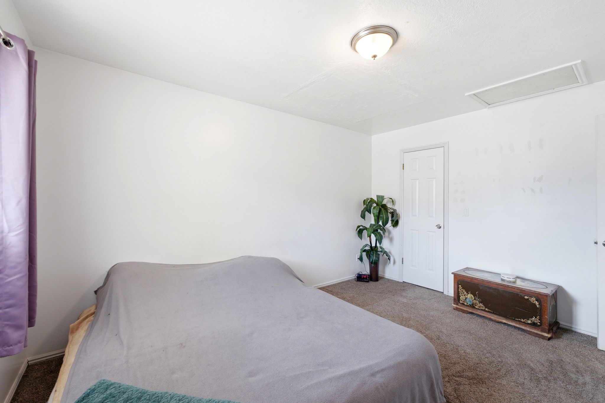 Carpeted room with a ceiling-mounted light fixture, white interior door, and a rectangular ceiling vent