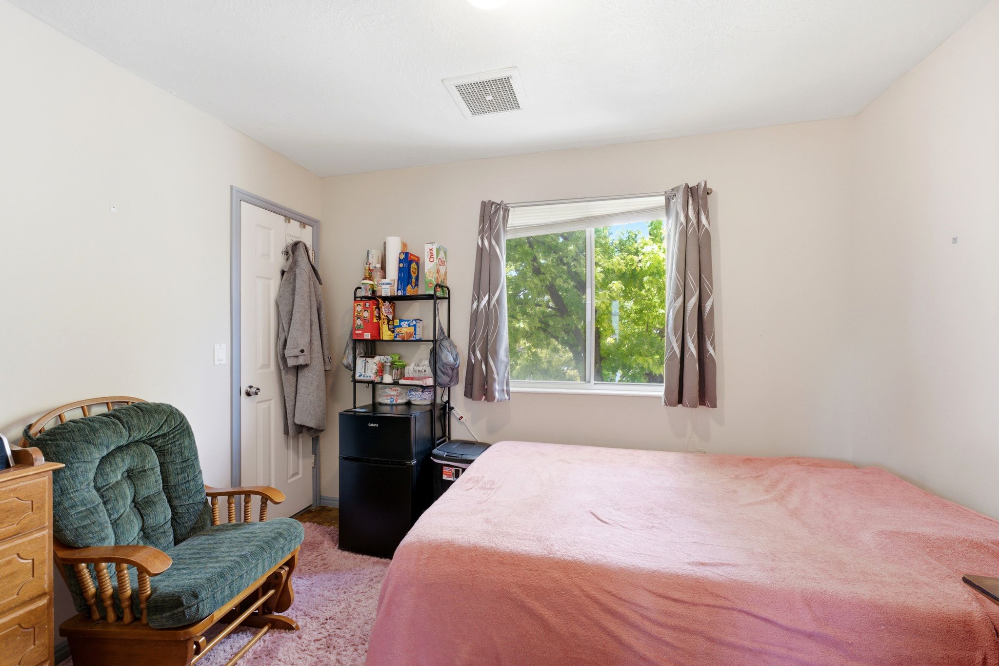Room featuring a window with exterior tree views, white walls, and a white ceiling with a visible vent