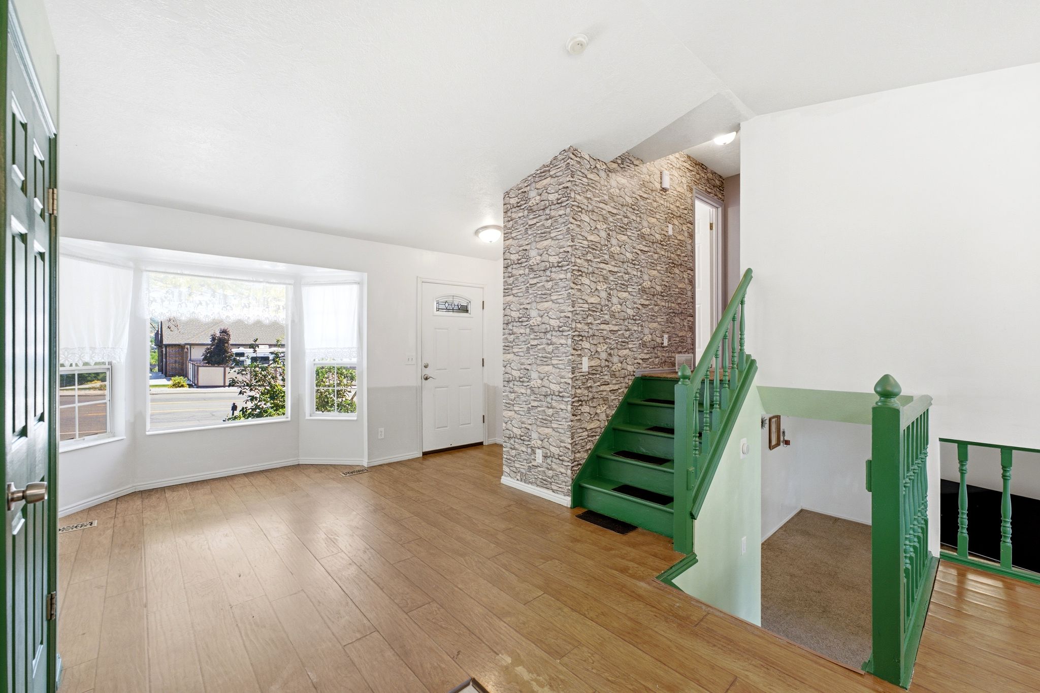 Bright entryway featuring wood-finish flooring, a bay window with natural light, a textured accent wall, and a staircase with green railings
