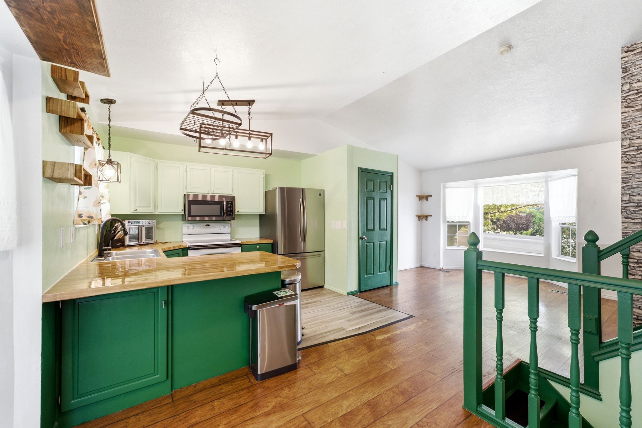 Vaulted ceiling open-concept kitchen featuring light-toned upper cabinetry, green lower cabinetry, and wood-finish countertops