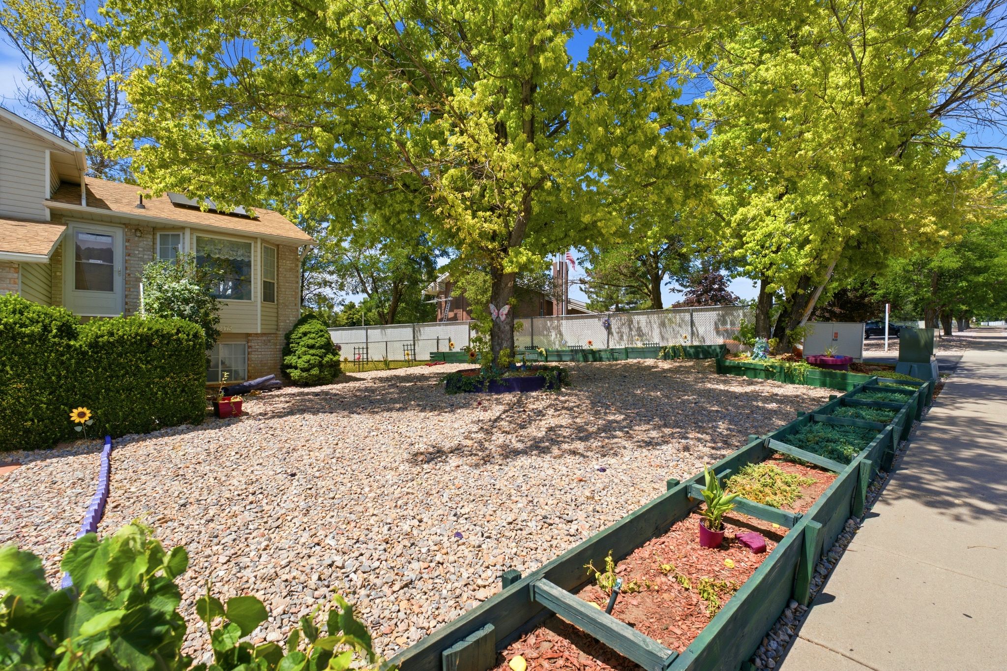 Spacious front yard featuring gravel landscaping, mature trees, and raised garden beds