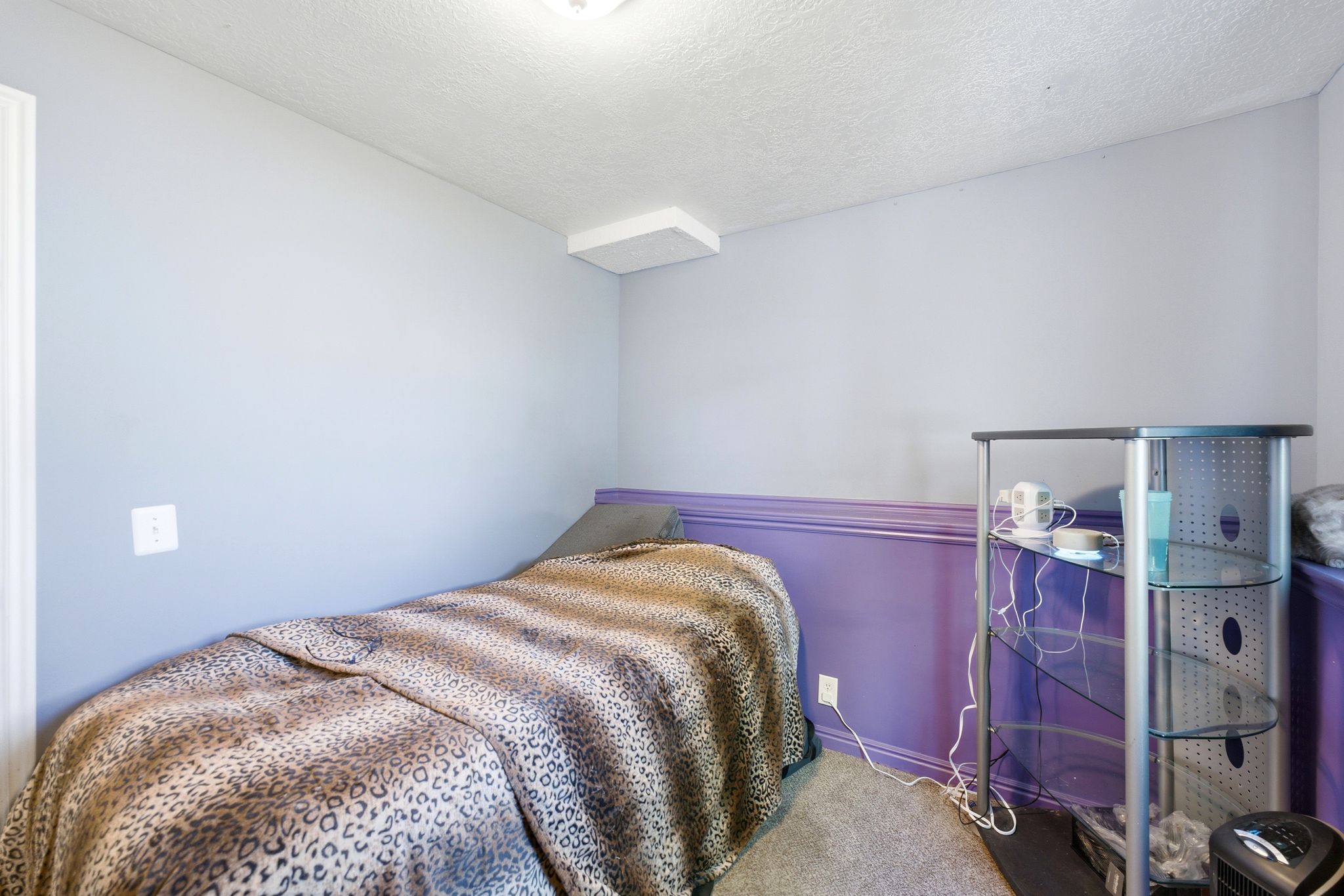 Compact room featuring a textured ceiling and light-toned walls with a purple wainscoting accent