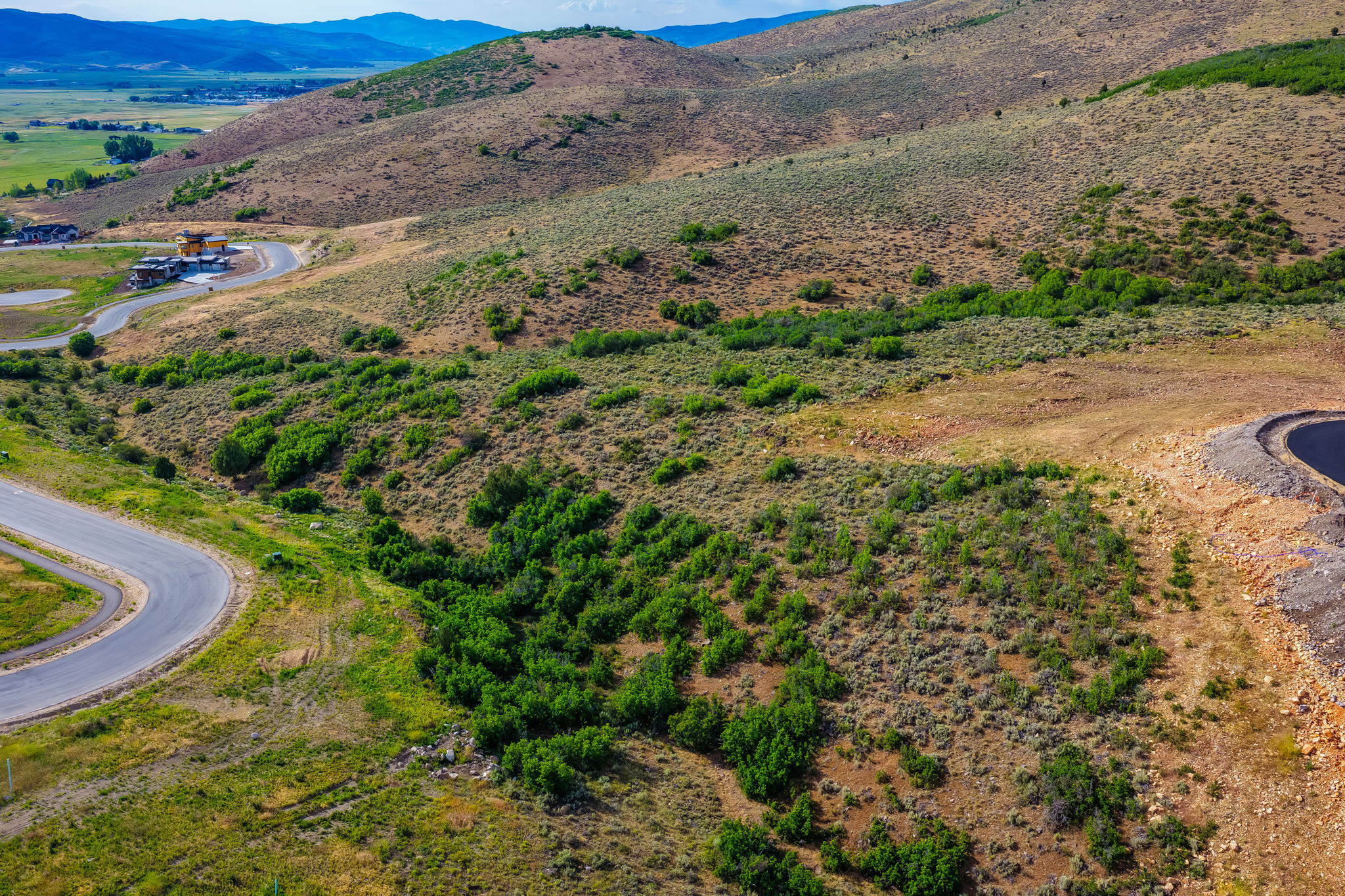 Sloping terrain featuring natural vegetation, winding paved roads, and distant mountain ranges