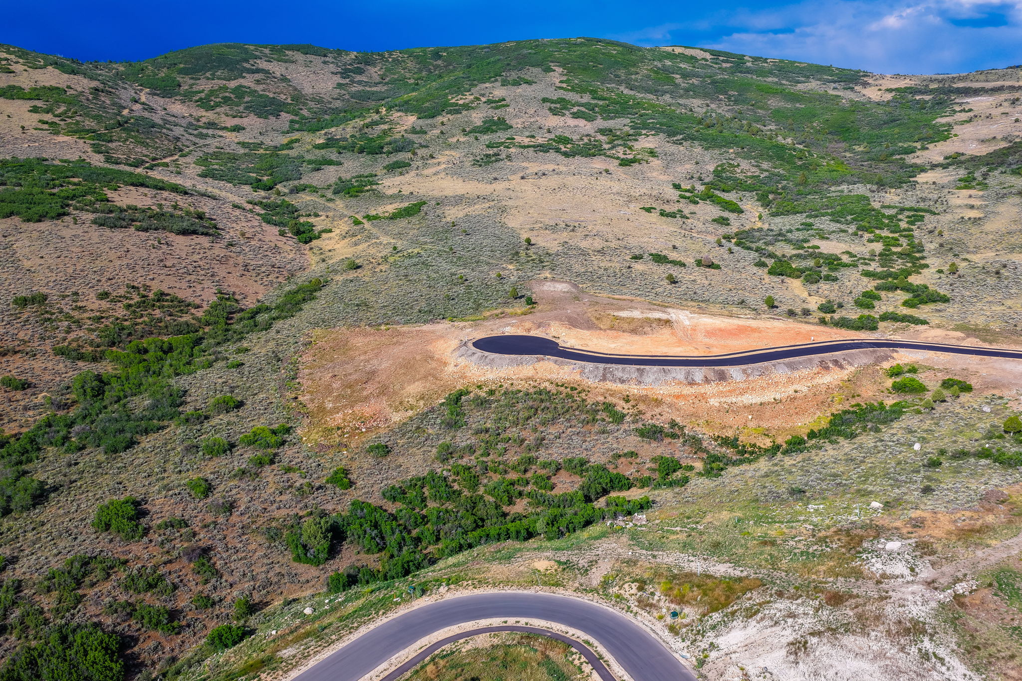 Hillside terrain with natural vegetation, featuring a newly paved asphalt road and a cul-de-sac