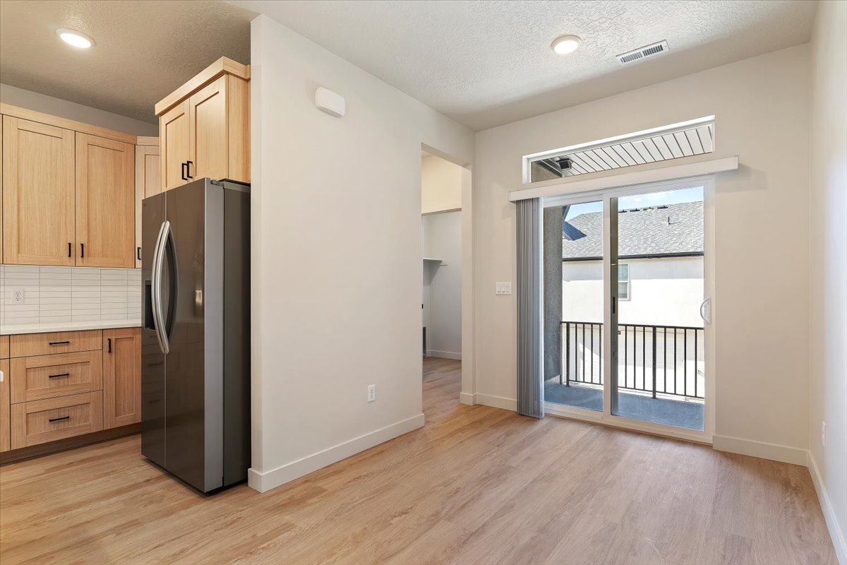 Contemporary kitchen and dining area featuring wood-finish flooring, light-toned cabinetry with dark hardware, and a stainless steel refrigerator