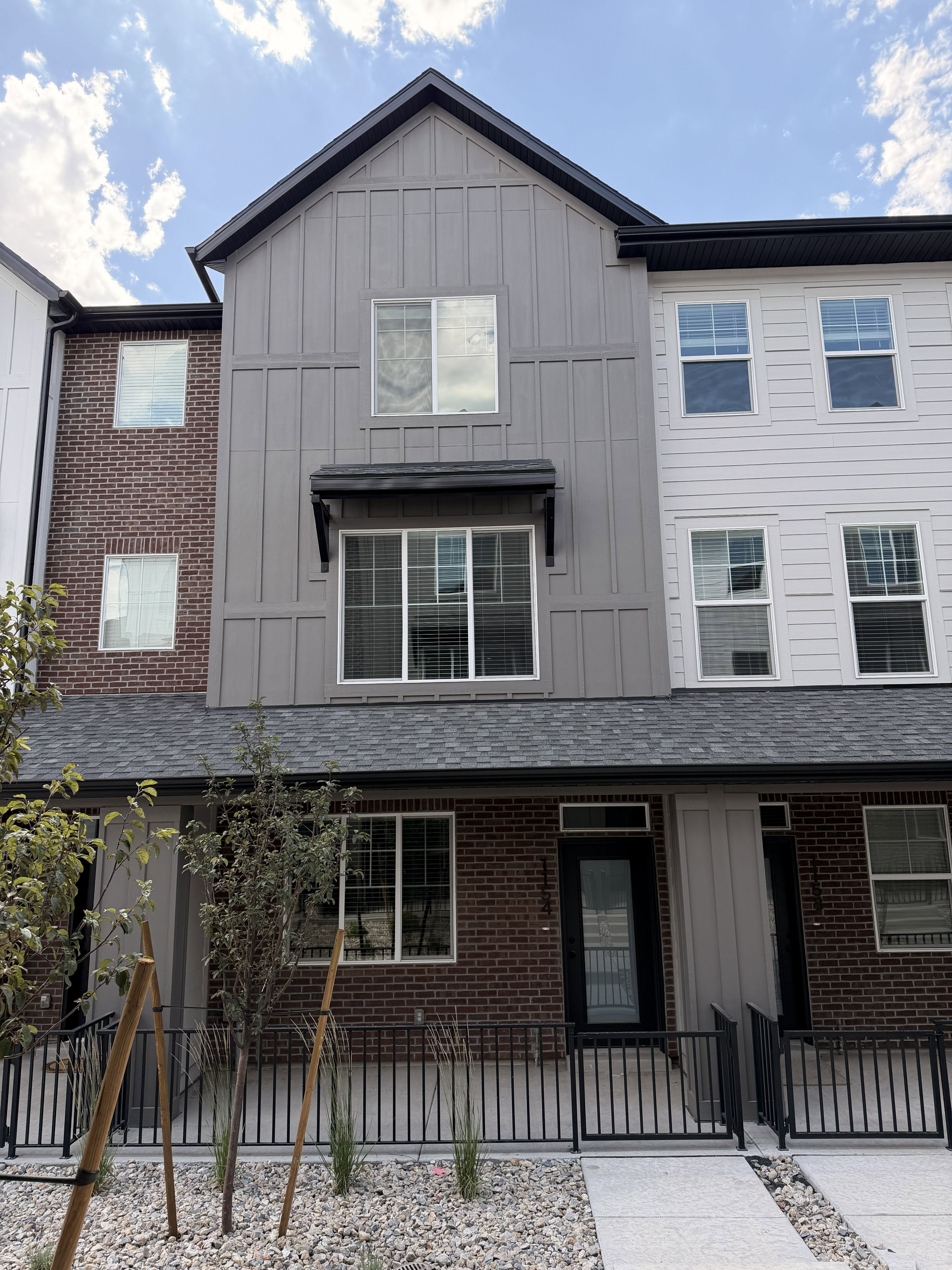 Modern townhome exterior featuring a multi-textured facade with dark brick, light siding, and board-and-batten accents