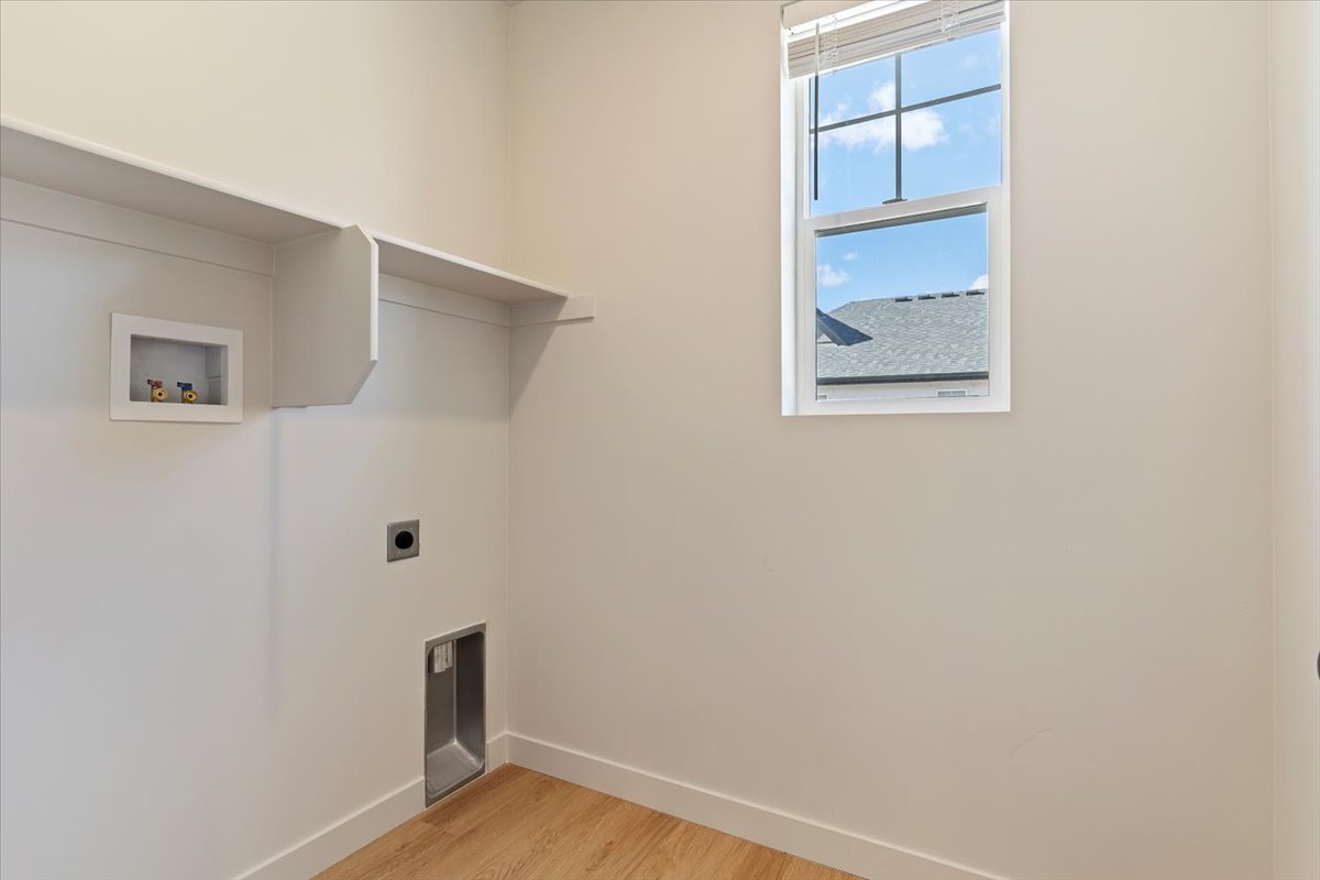 Laundry area with wood-finish flooring, built-in shelving, and a window for natural light