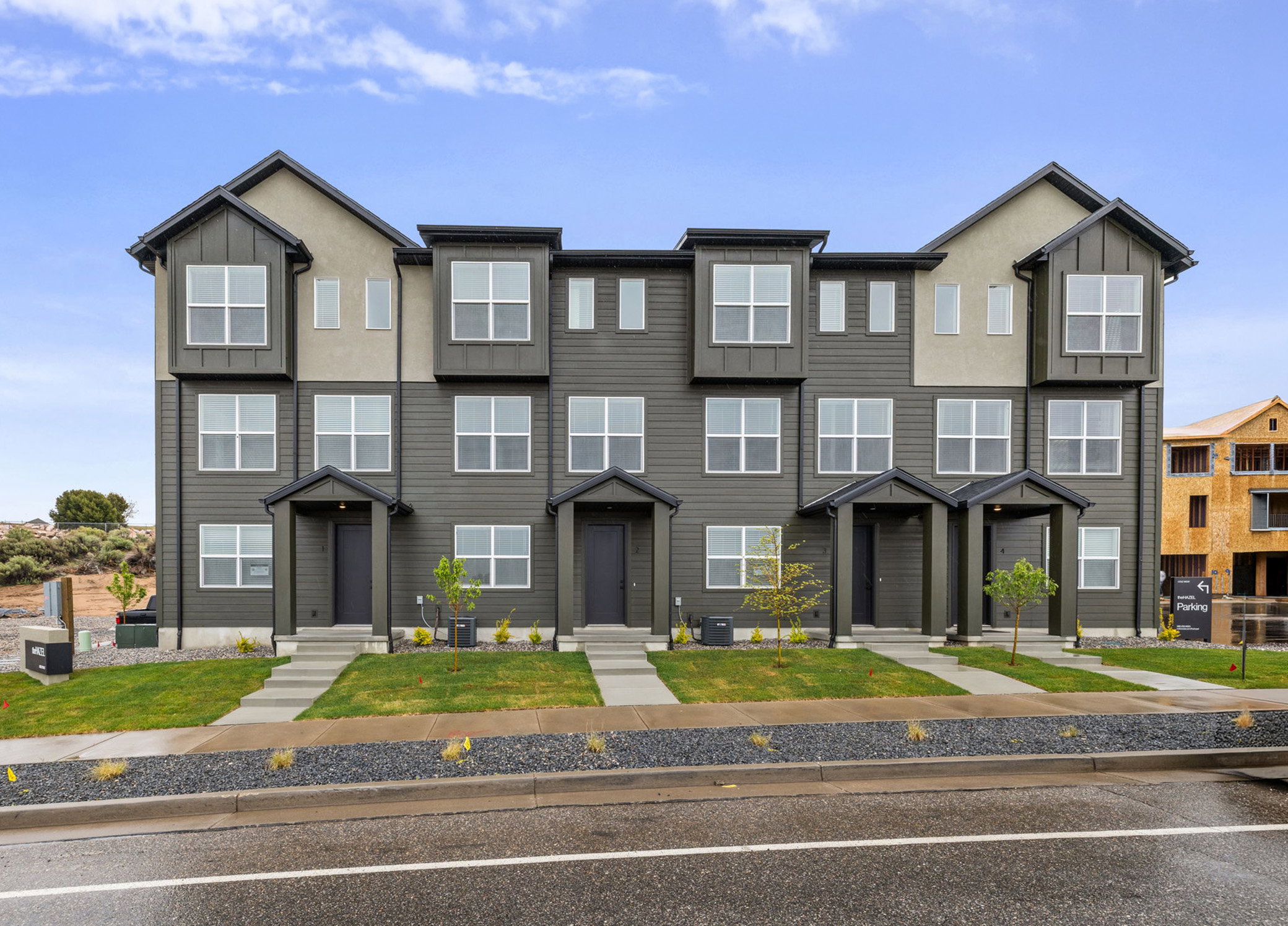 Modern townhome exterior featuring multi-toned siding, gabled rooflines, multiple window styles, covered entryways, and a concrete walkway with manicured landscaping