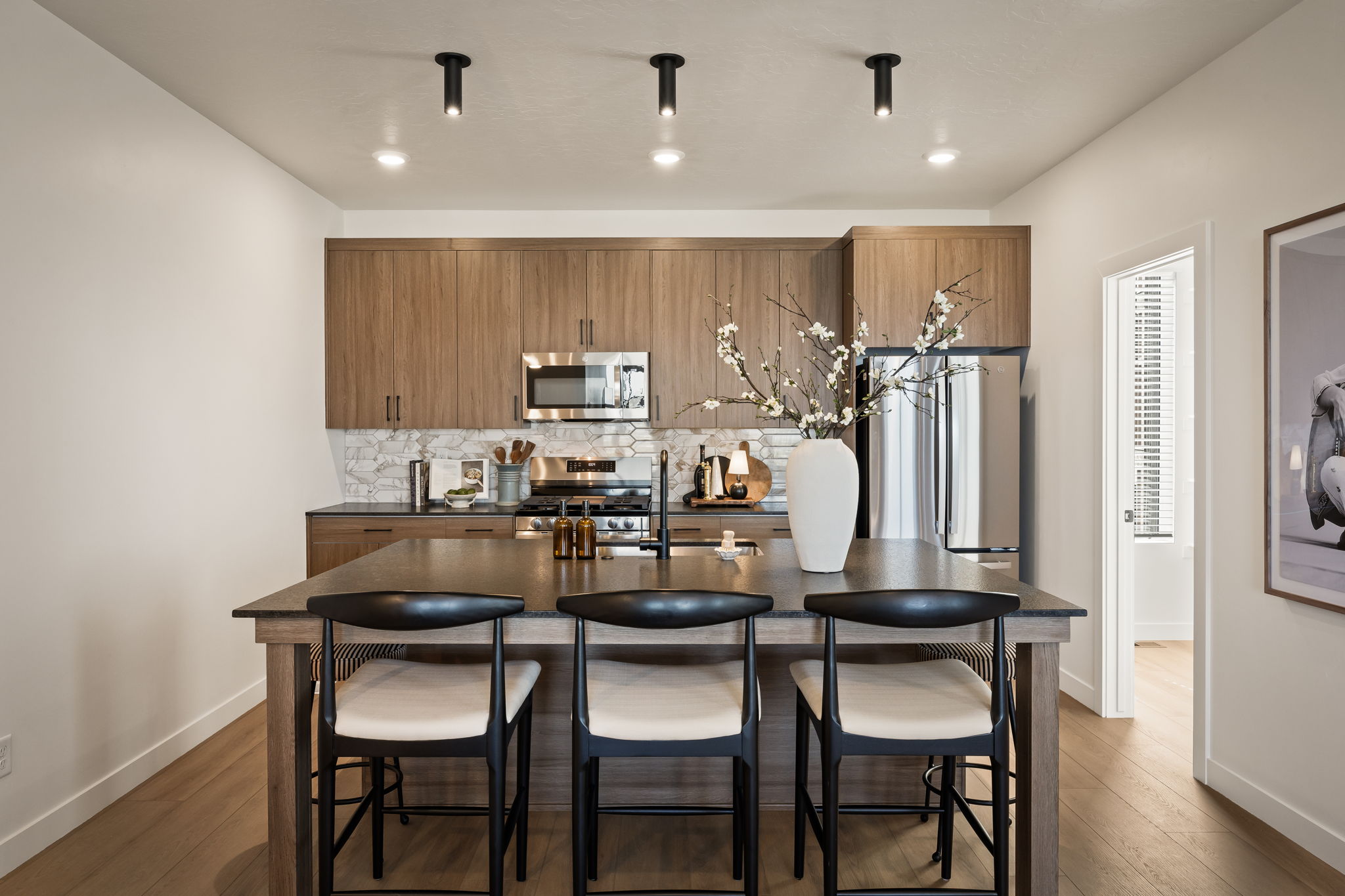Kitchen featuring a central island with seating for three, stainless steel appliances, wood-finish cabinetry, a patterned tile backsplash, and overhead track lighting