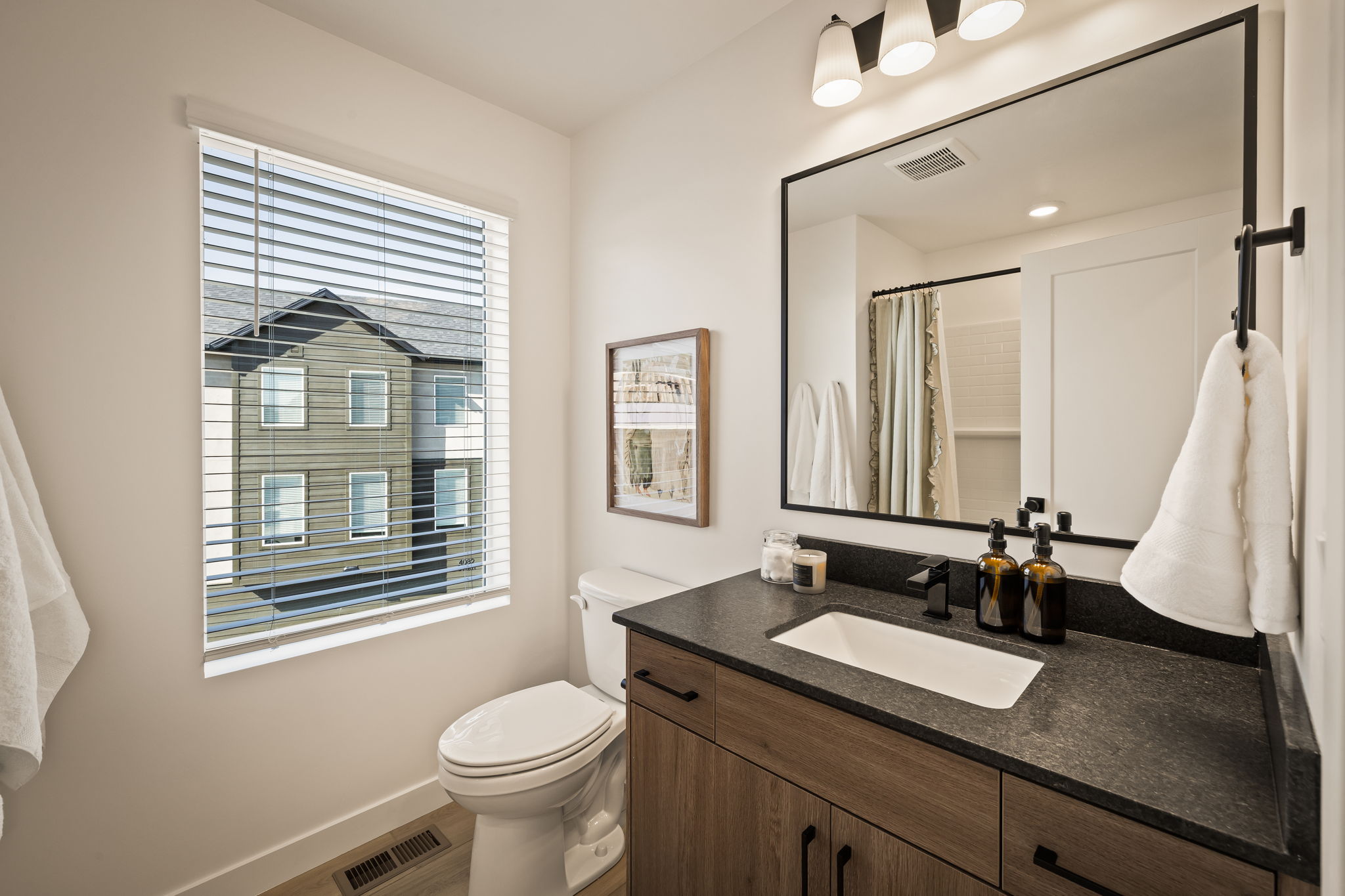 Modern bathroom featuring a wood-finish vanity with a dark countertop, undermount sink, and black wall-mounted faucet