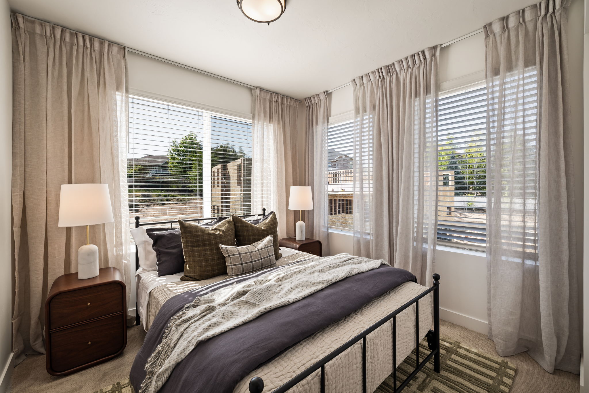 Bedroom featuring a wall of multiple windows with horizontal blinds and floor-length drapery